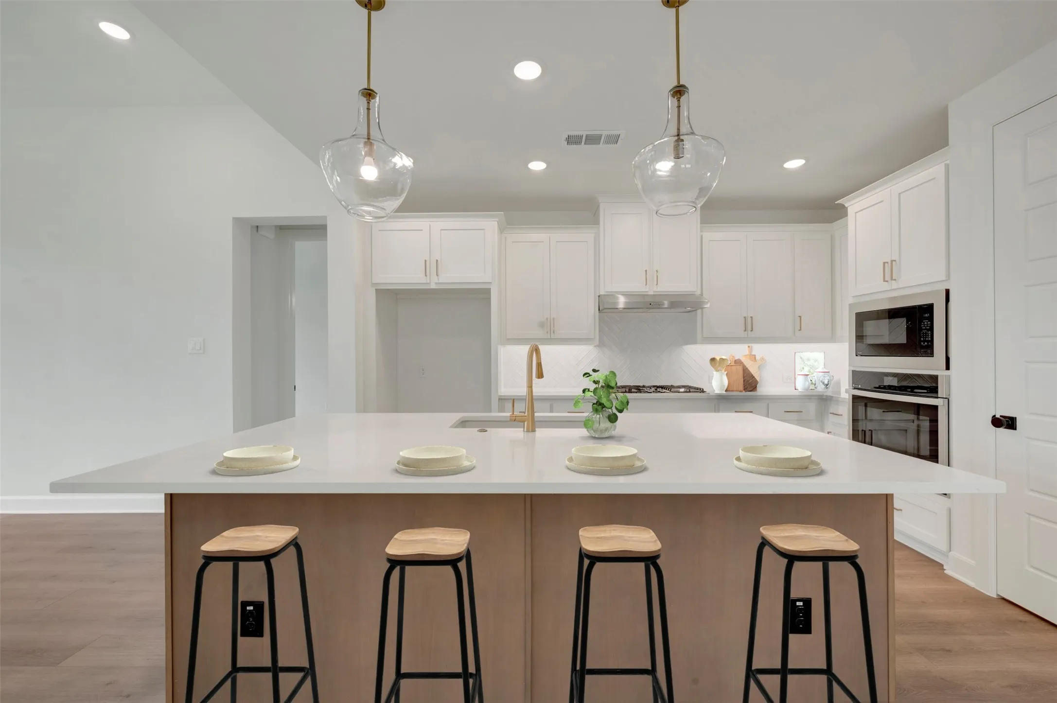 Kitchen featuring a large center island, white cabinetry, integrated stainless steel appliances, and wood-finish flooring