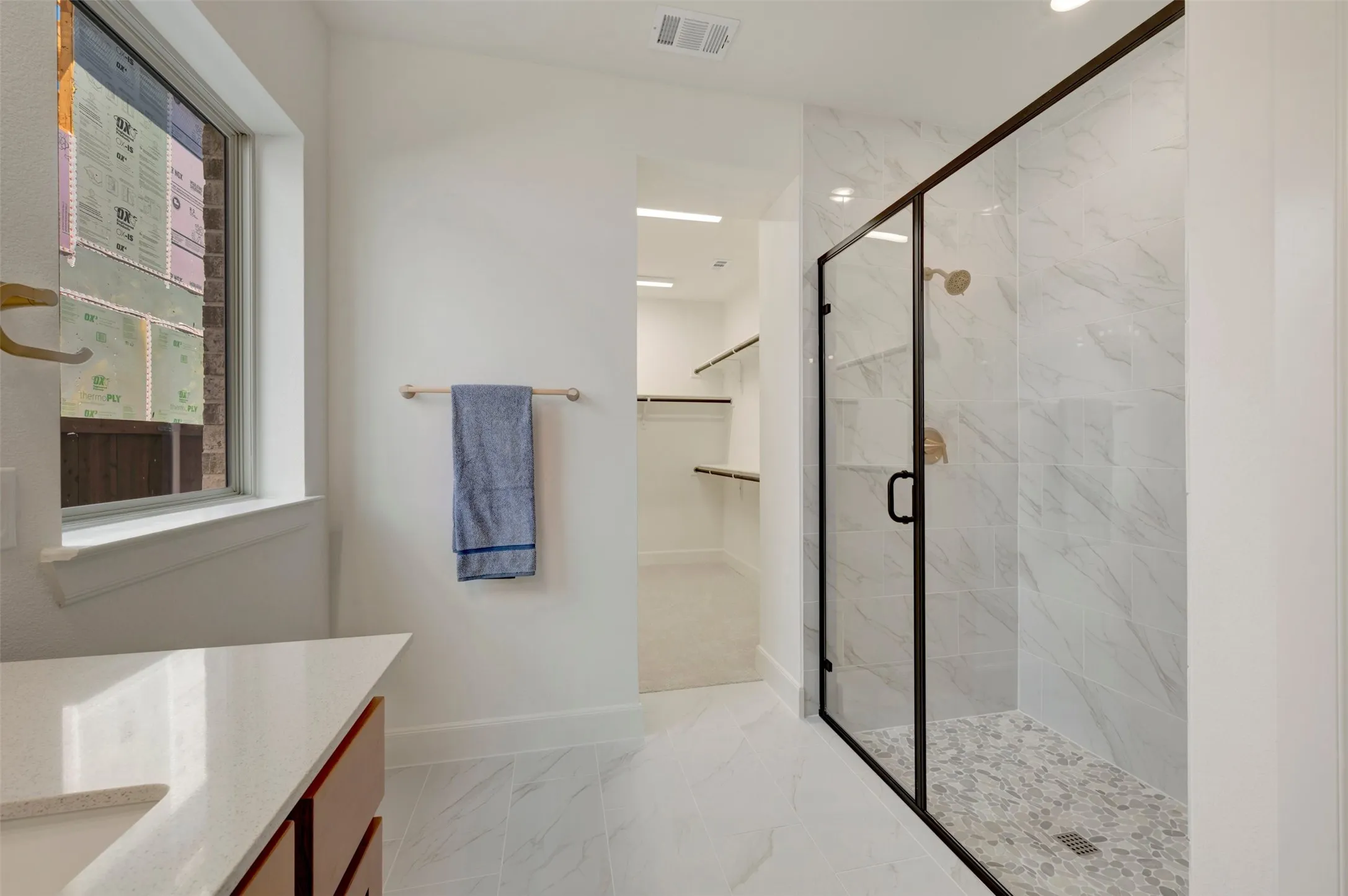 Walk-in shower with black-framed glass enclosure, white marble-style tile walls, and pebble-finish floor