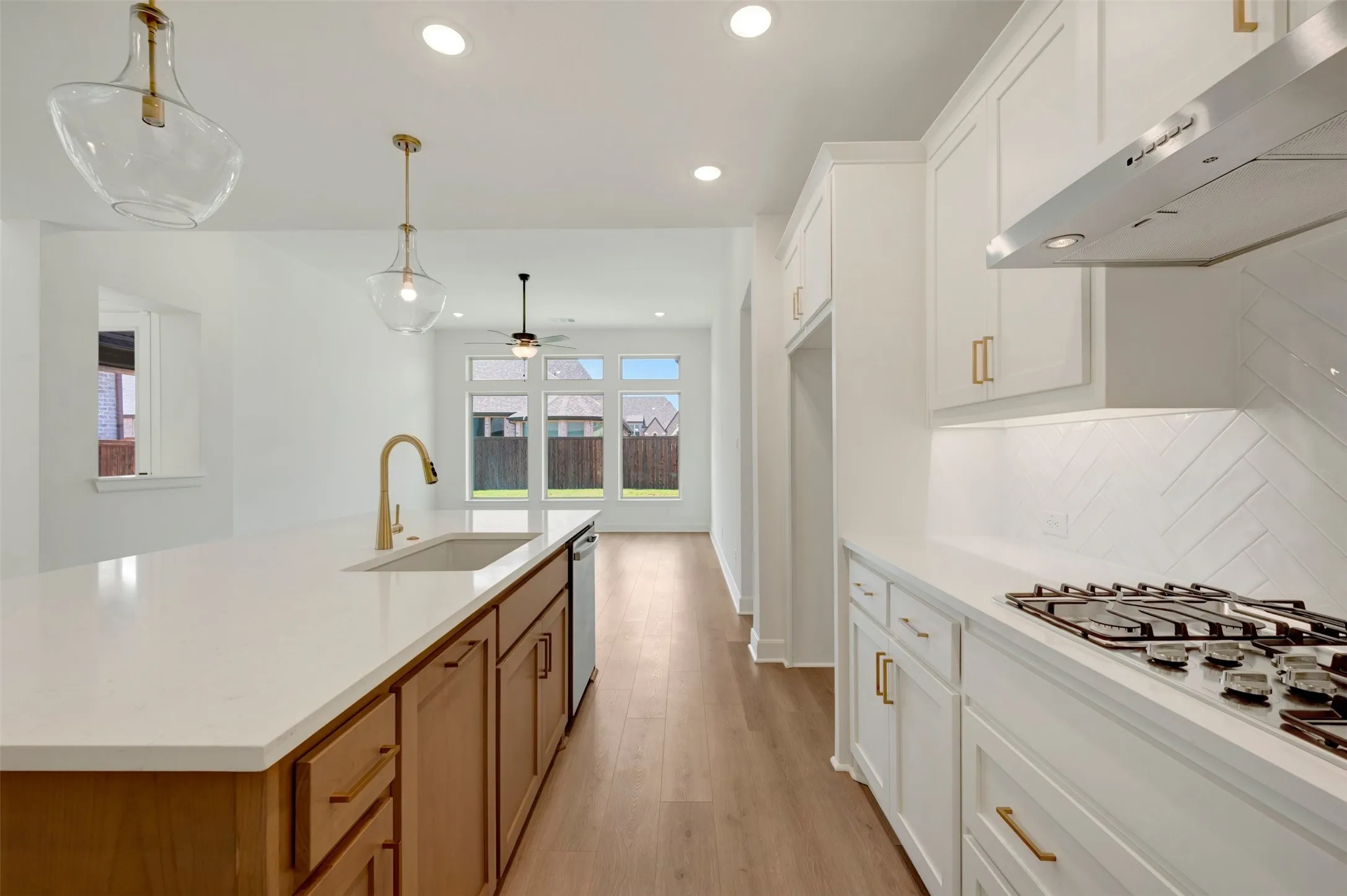 Kitchen featuring white shaker cabinetry, wood-finish flooring, a kitchen island with integrated sink, stainless steel appliances, and herringbone tile backsplash