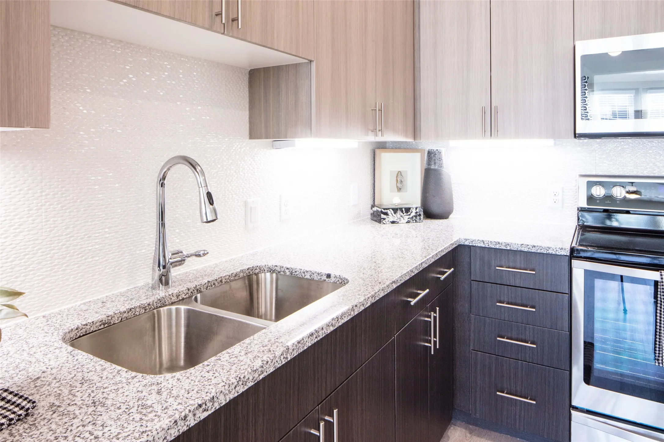 Kitchen with dark brown cabinets, stainless steel appliances, light stone countertops, and sink
