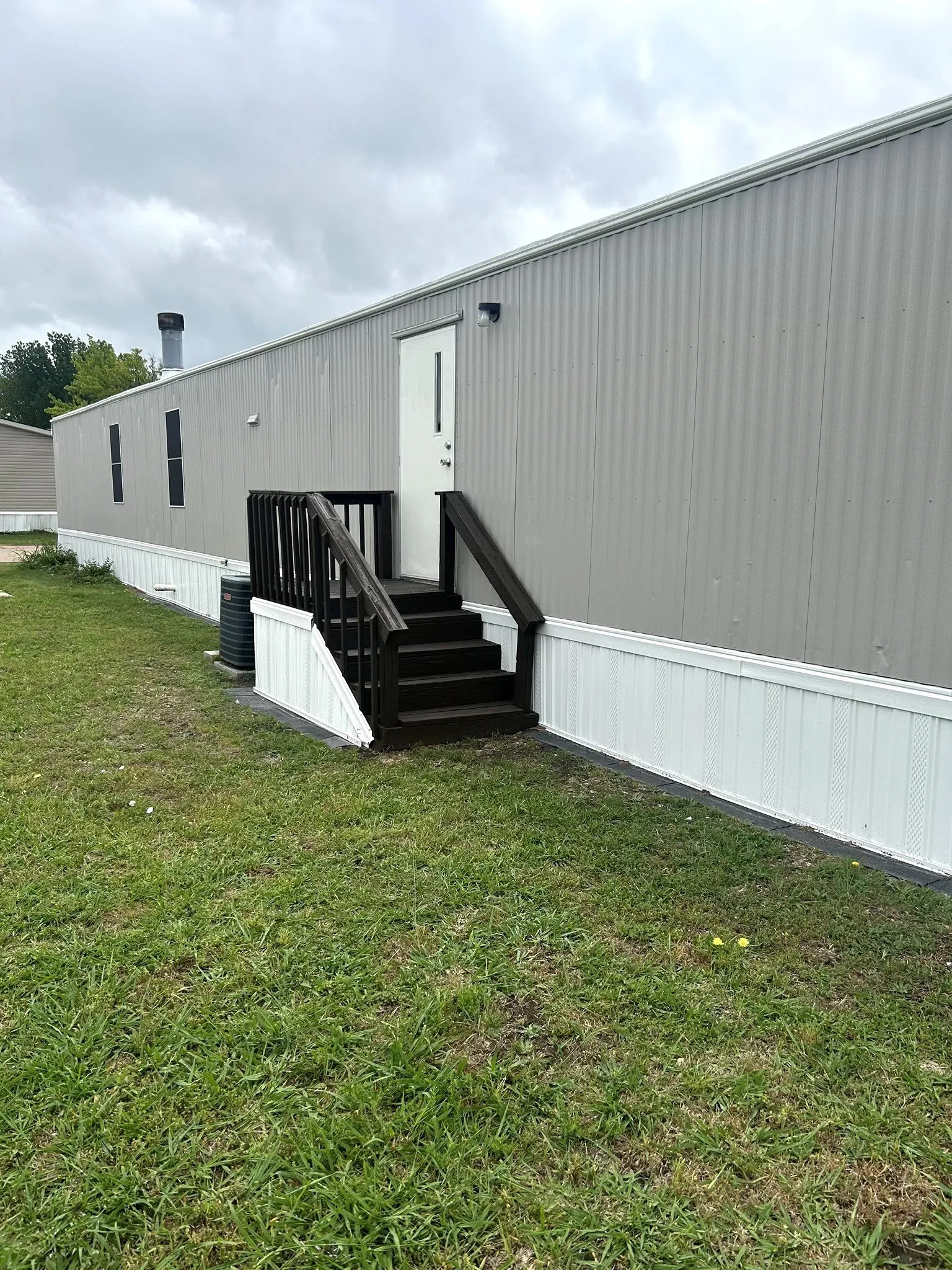 Gray corrugated metal siding with white trim, featuring a dark brown wood staircase and railing leading to a white entry door