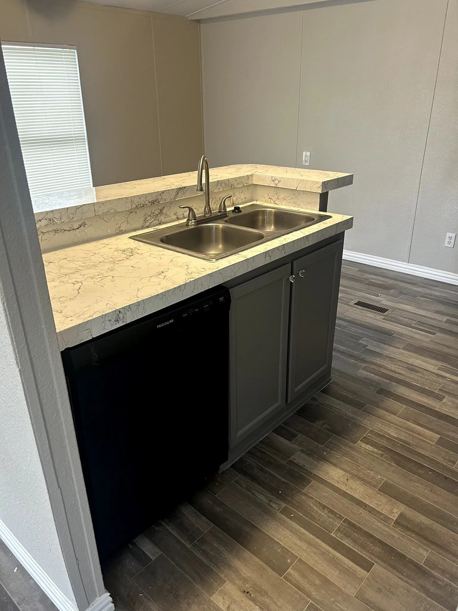 Kitchen area featuring a double basin stainless steel sink, a black dishwasher, light-toned countertops with a raised bar, and gray cabinetry
