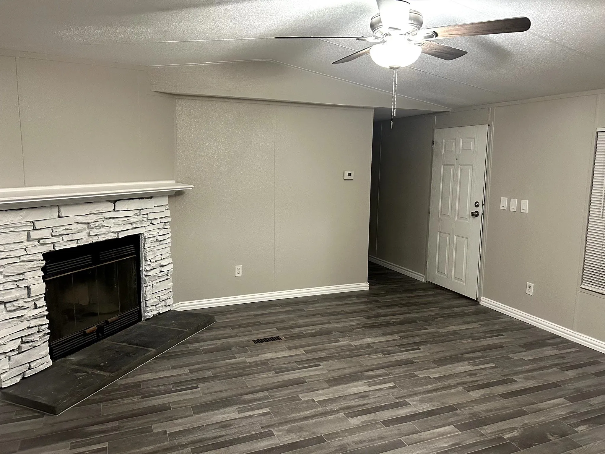 Living area featuring a stone-clad fireplace with hearth, wood-finish flooring, a ceiling fan with integrated lighting, and neutral wall tones