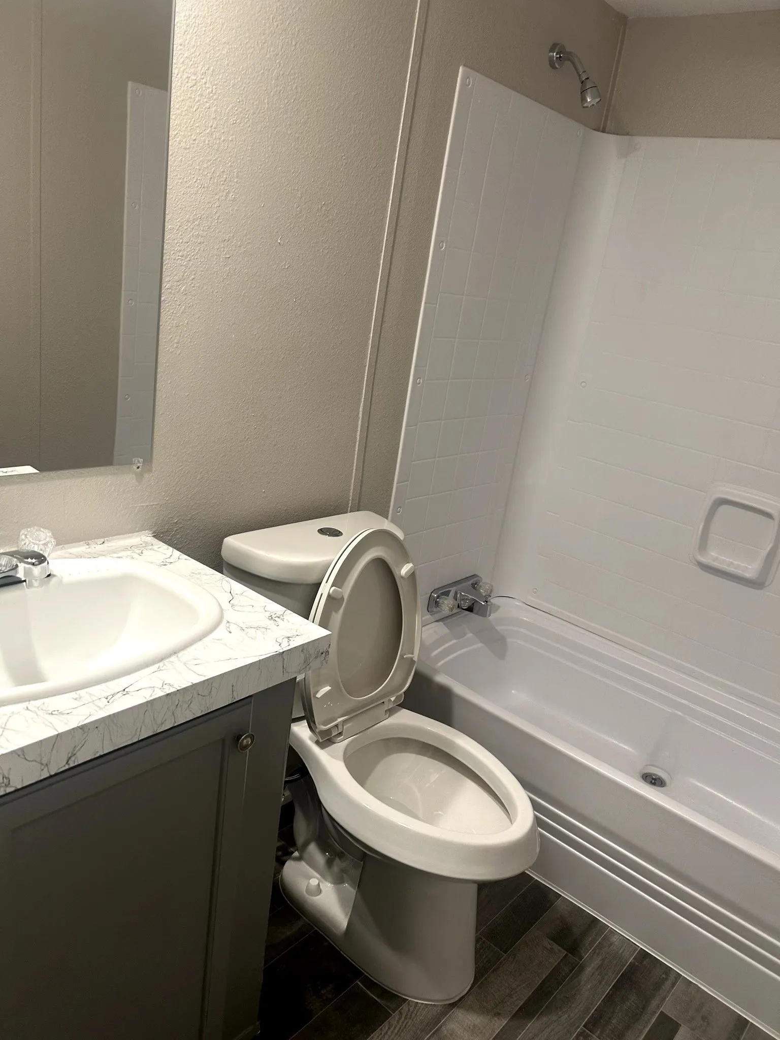 Bathroom featuring a bathtub/shower combination with white surround, a toilet, and a vanity with a white basin and a stone-look countertop