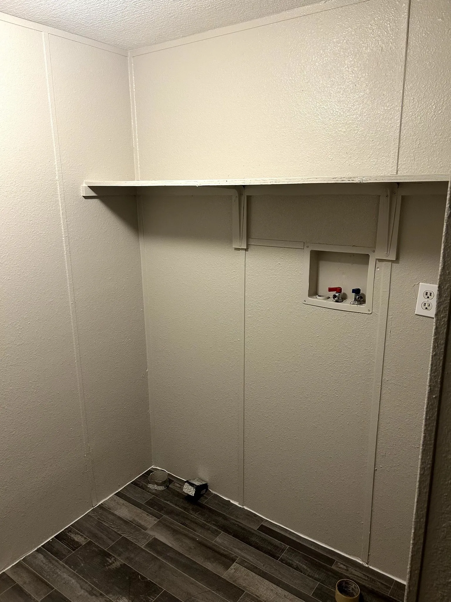 Dedicated utility space featuring durable wood-look flooring, light-toned wall paneling, and a built-in storage shelf