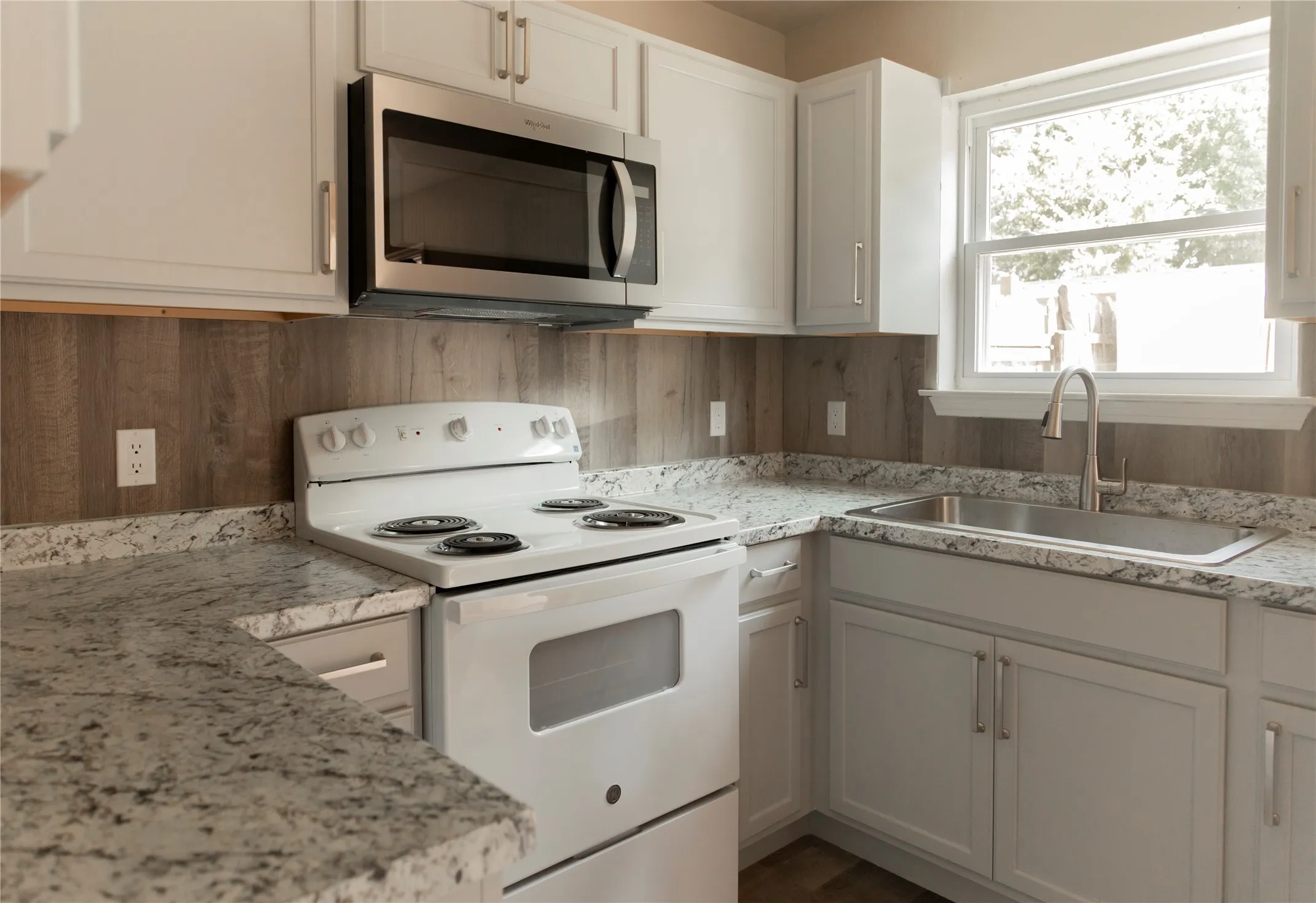 Kitchen featuring white cabinetry, stone-finish countertops, wood-look paneling backsplash, and a stainless steel over-the-range microwave