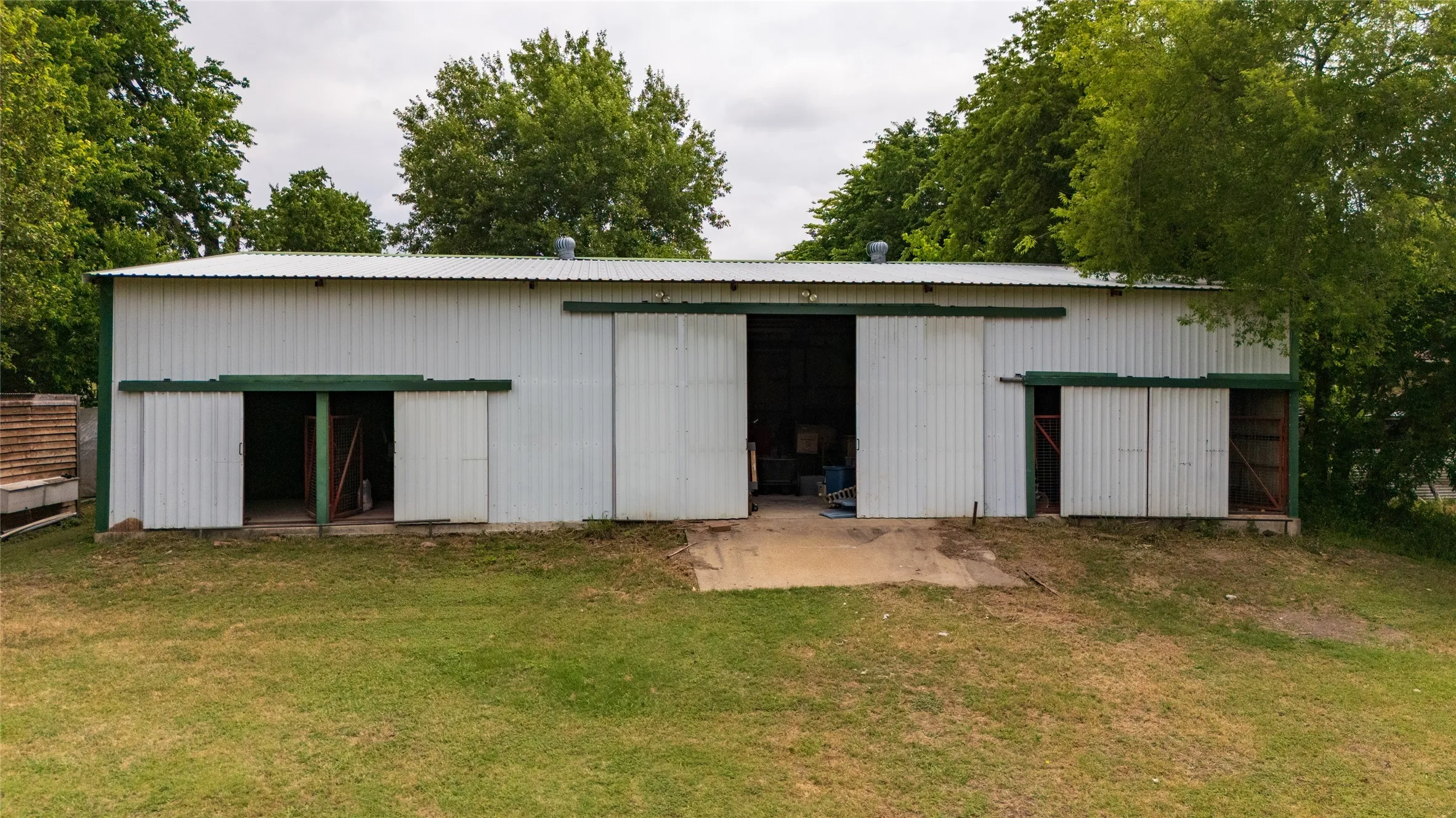 Expansive metal outbuilding featuring a corrugated roof, multiple sliding bay doors, and a concrete approach