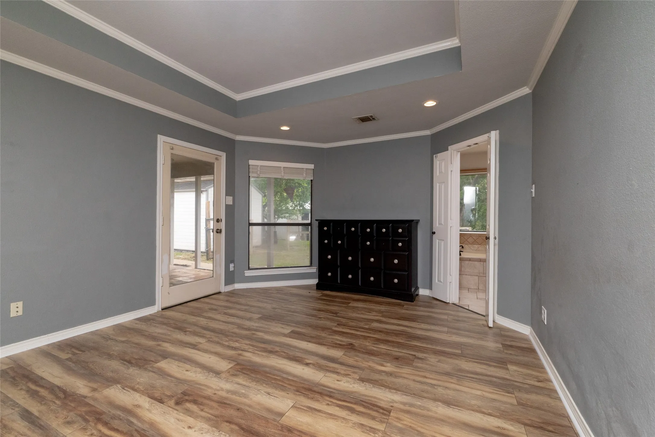 Spacious primary bedroom featuring wood-look flooring, a tray ceiling, door to patio and crown molding
