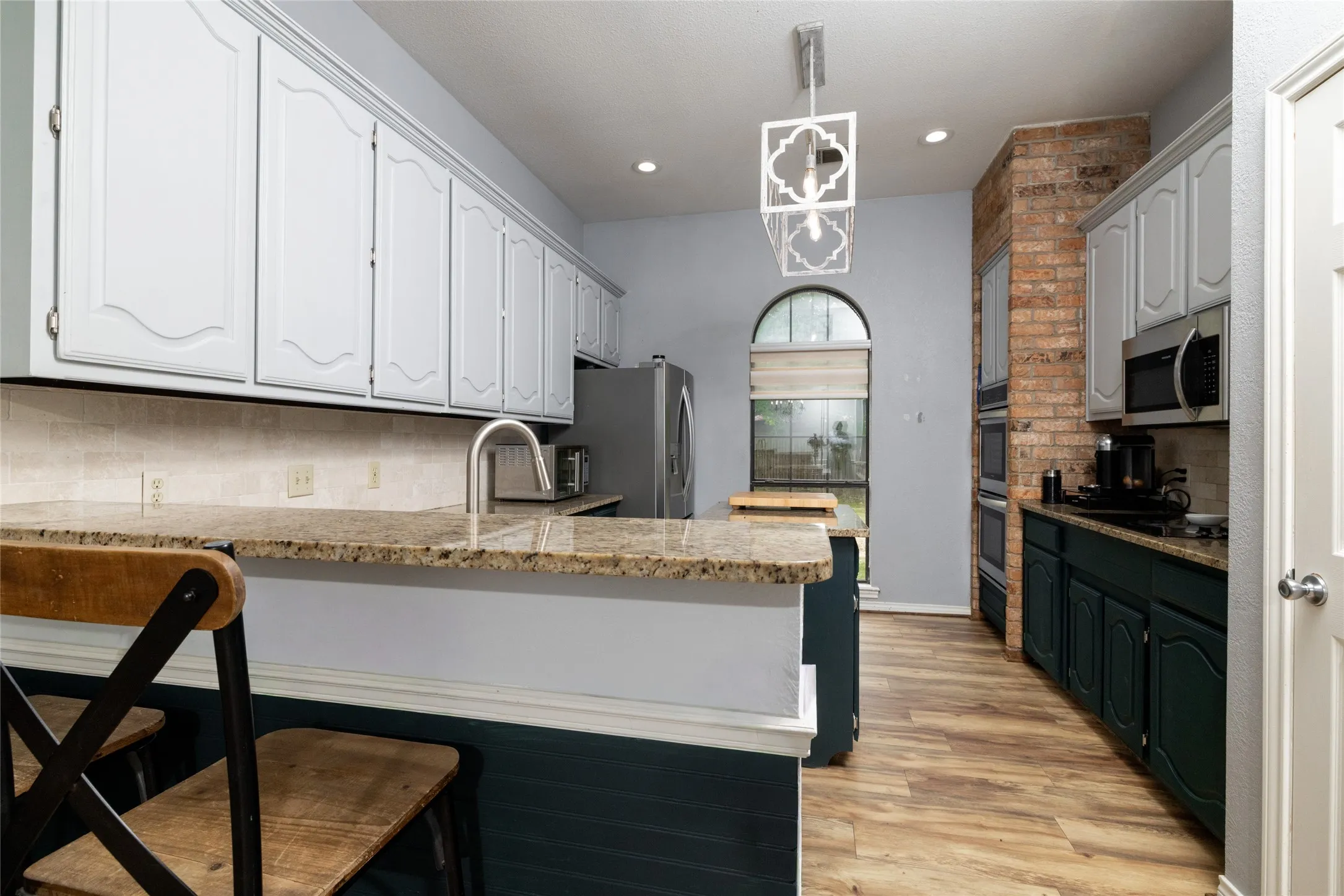 Kitchen featuring wood-look flooring, two-tone cabinetry, granite countertops, a tiled backsplash, and an arched window