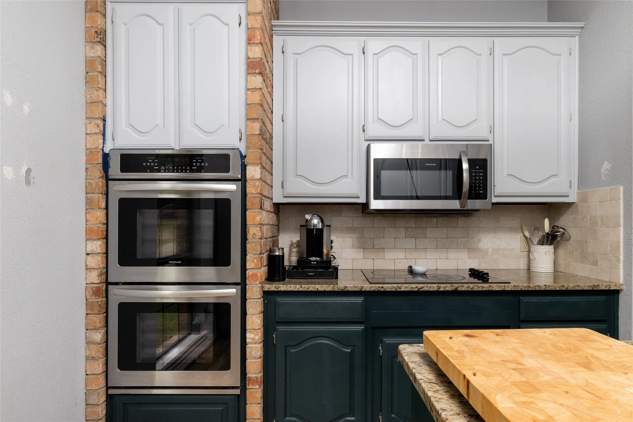 Kitchen featuring a built-in double oven, stainless steel microwave, granite countertops, and a tile backsplash