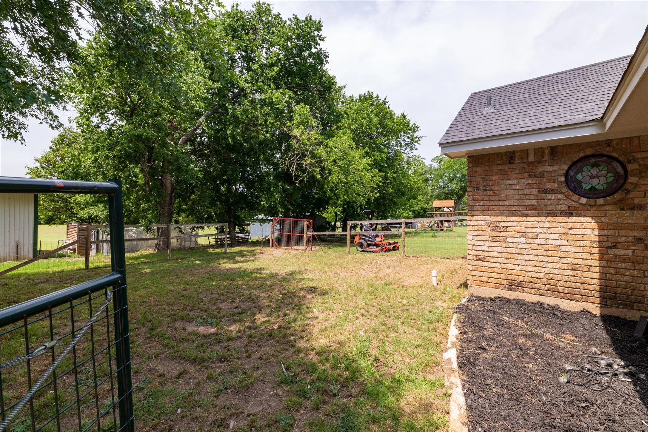 Expansive exterior grounds featuring a brick-clad structure with a shingled roof and a decorative stained glass window