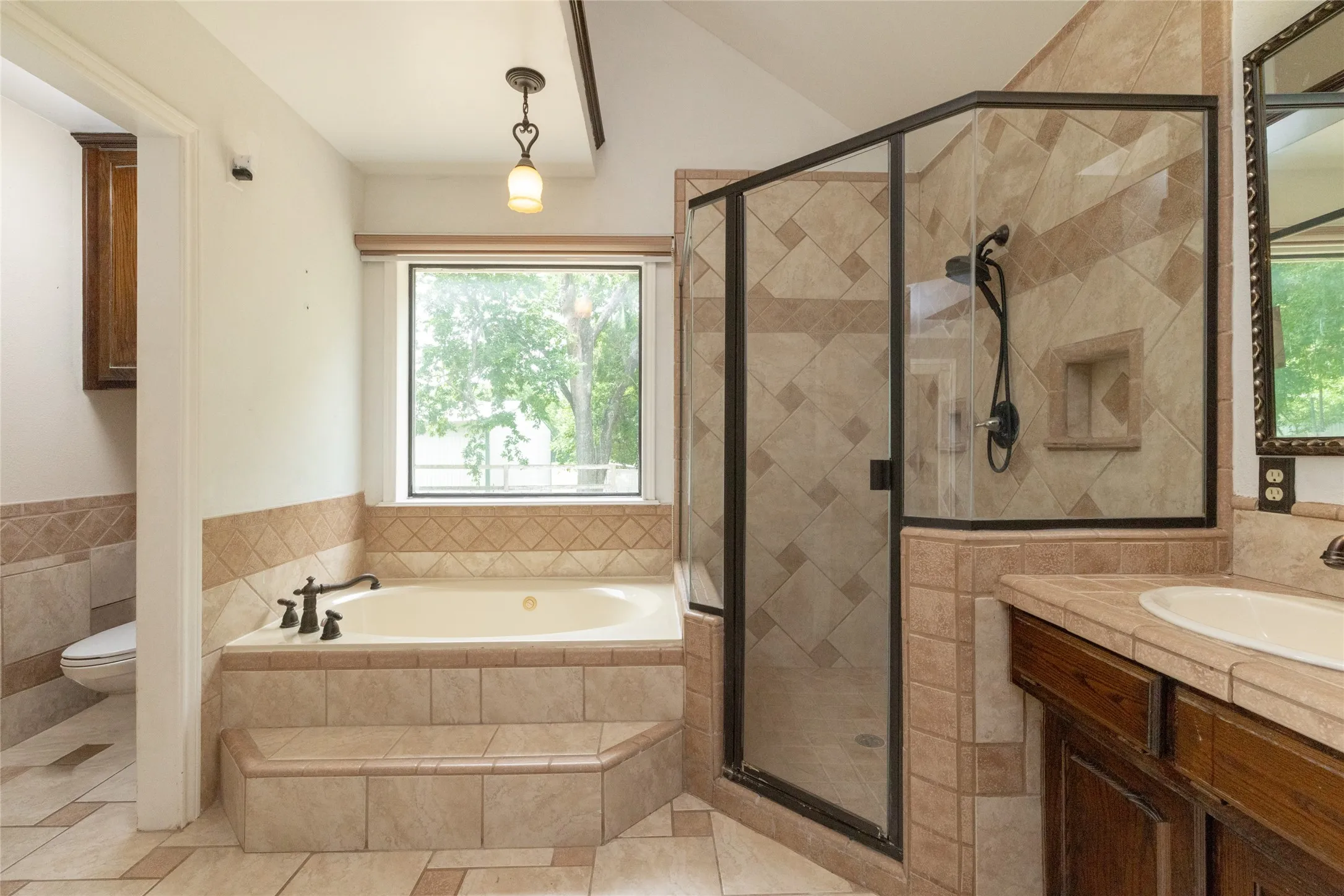 Tiled step-up soaking tub with a window, bronze-finish fixtures, and a glass-enclosed shower with a built-in niche