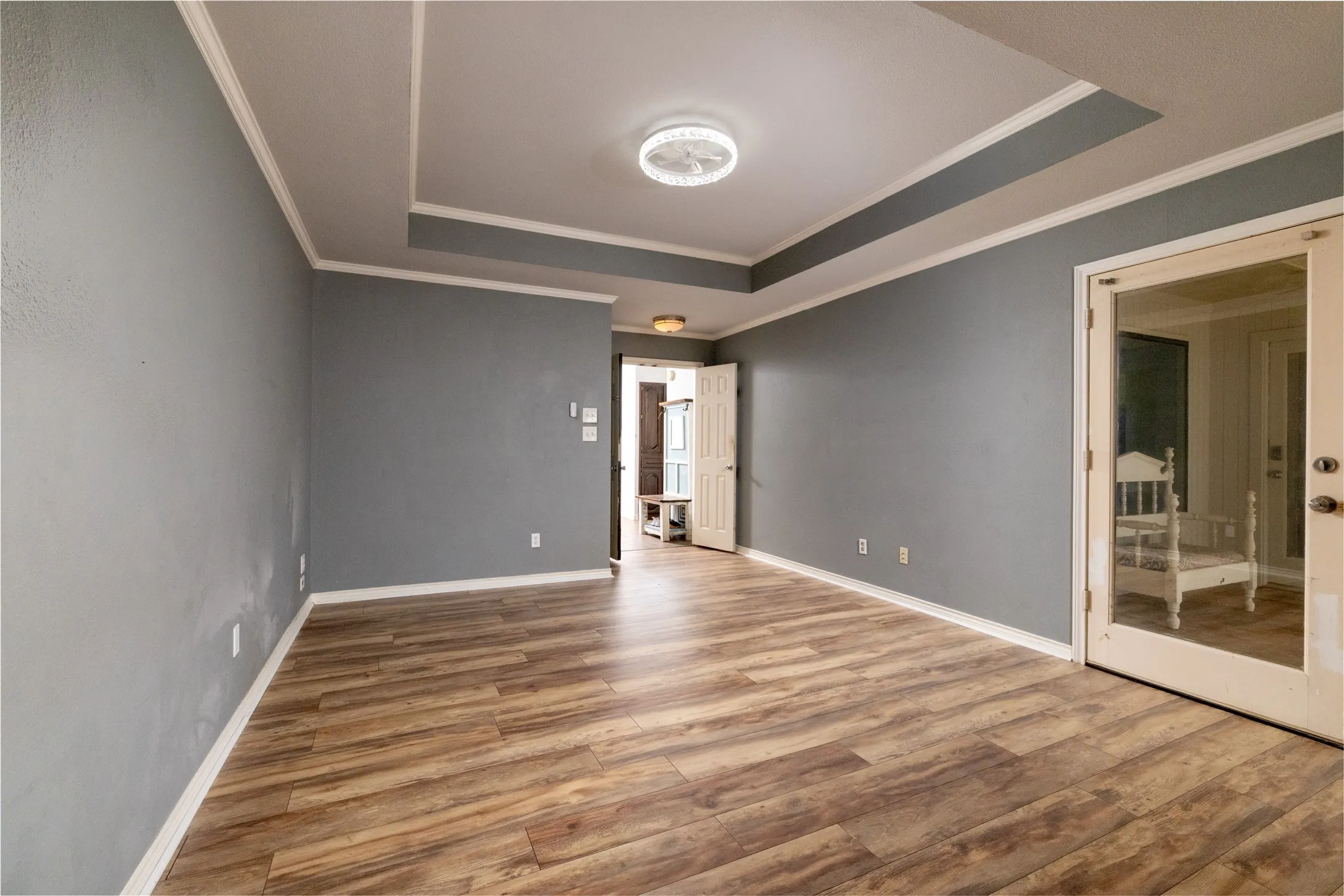 Spacious interior with wood-look flooring, tray ceiling with crown molding, and a flush mount light fixture