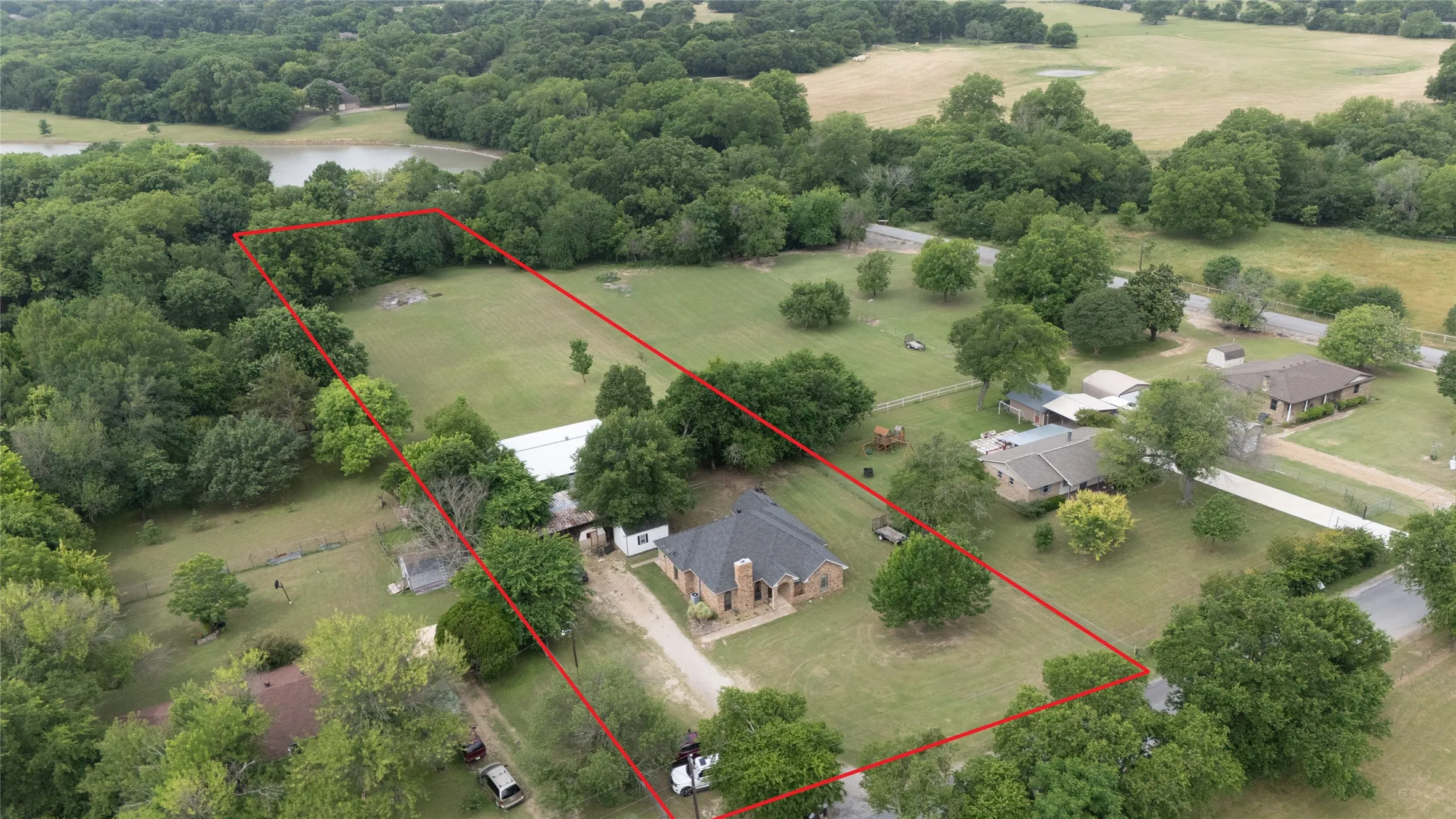 Expansive property featuring a brick residence with a dark shingle roof, mature landscaping, and a substantial portion of open land