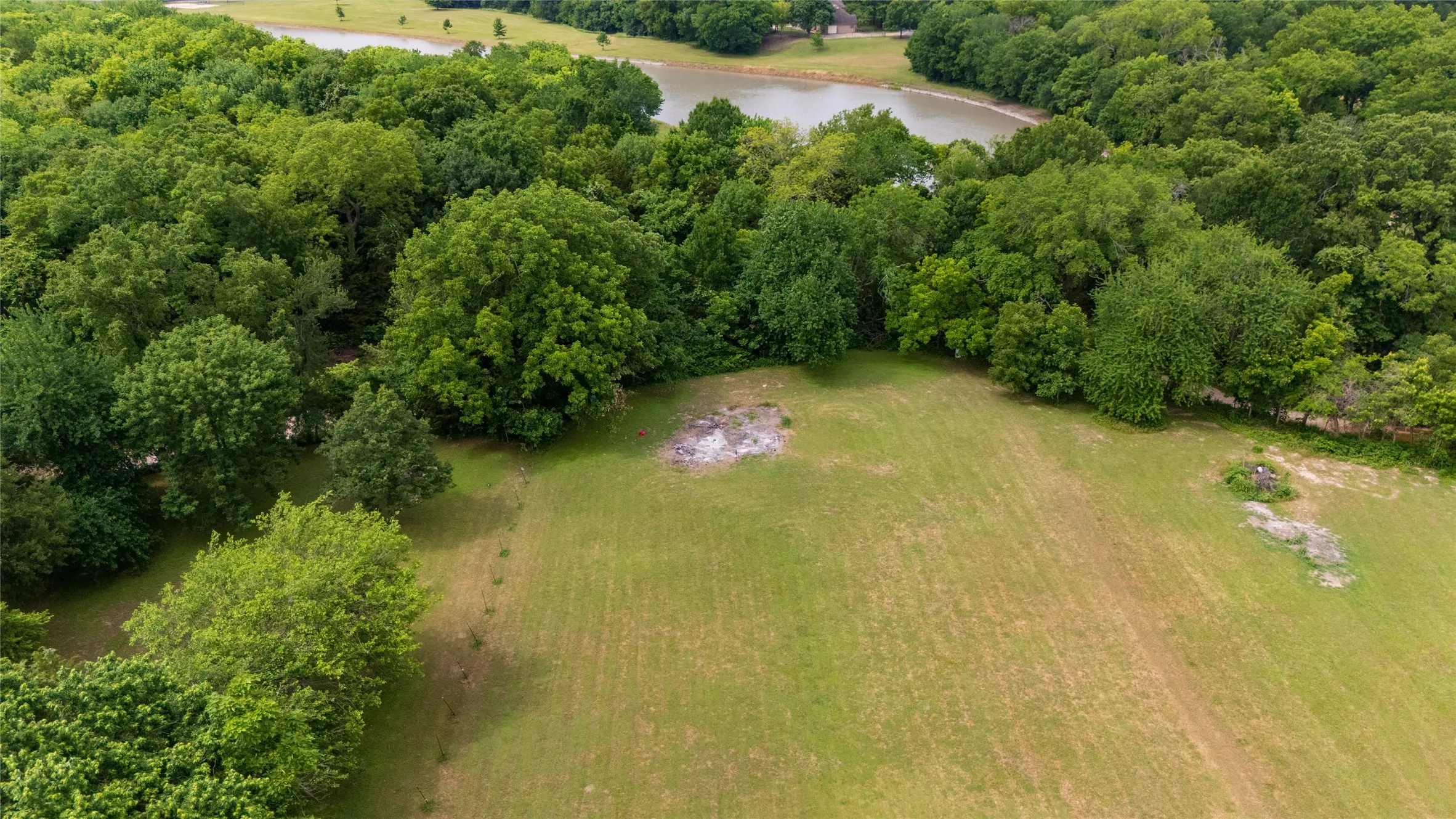 Expansive undeveloped lot featuring a large grassy area, abundant mature trees, and a distant body of water