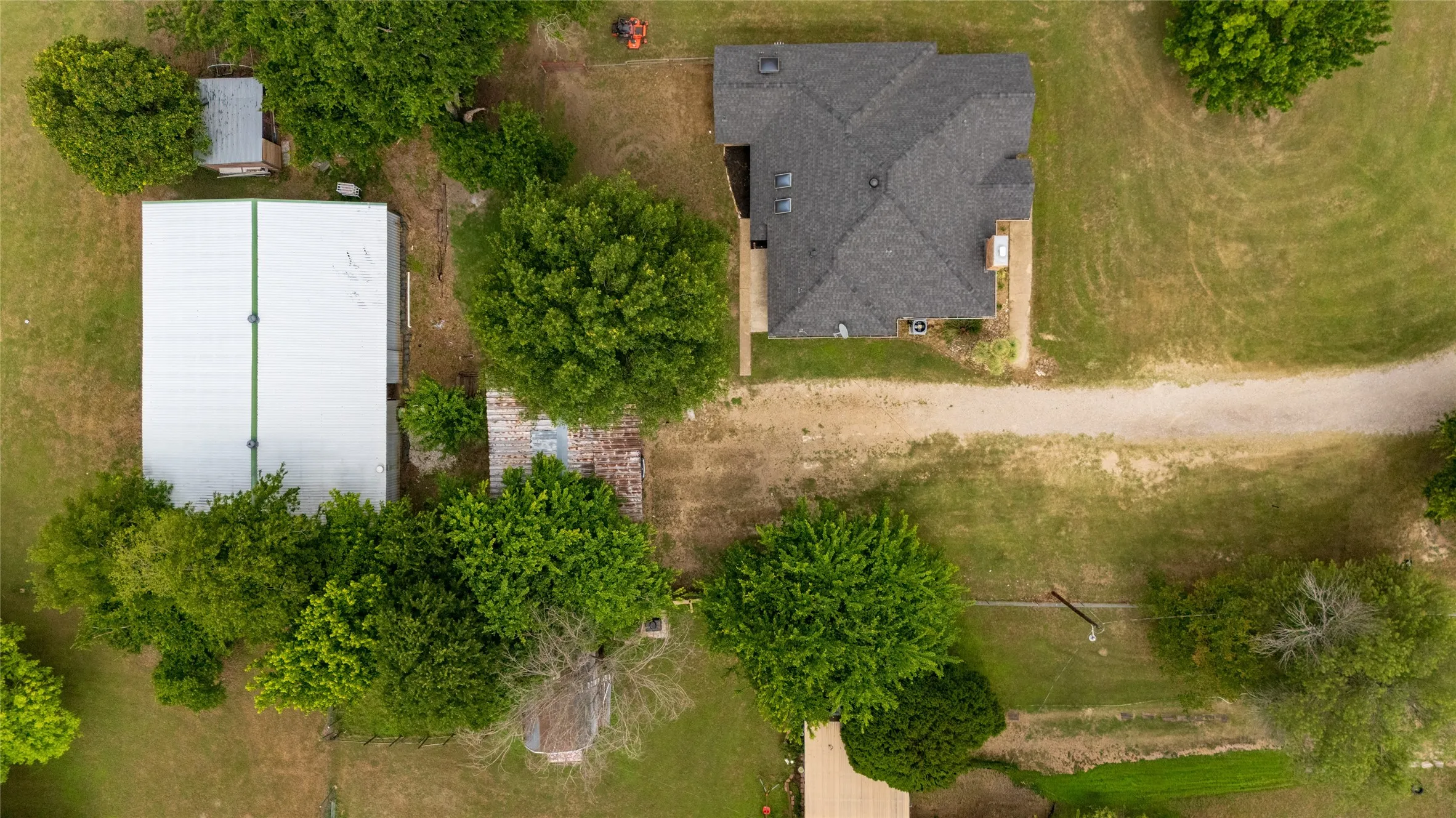 Expansive property featuring a main residence with a dark shingle roof, a large metal-roofed outbuilding, and significant green space with mature trees
