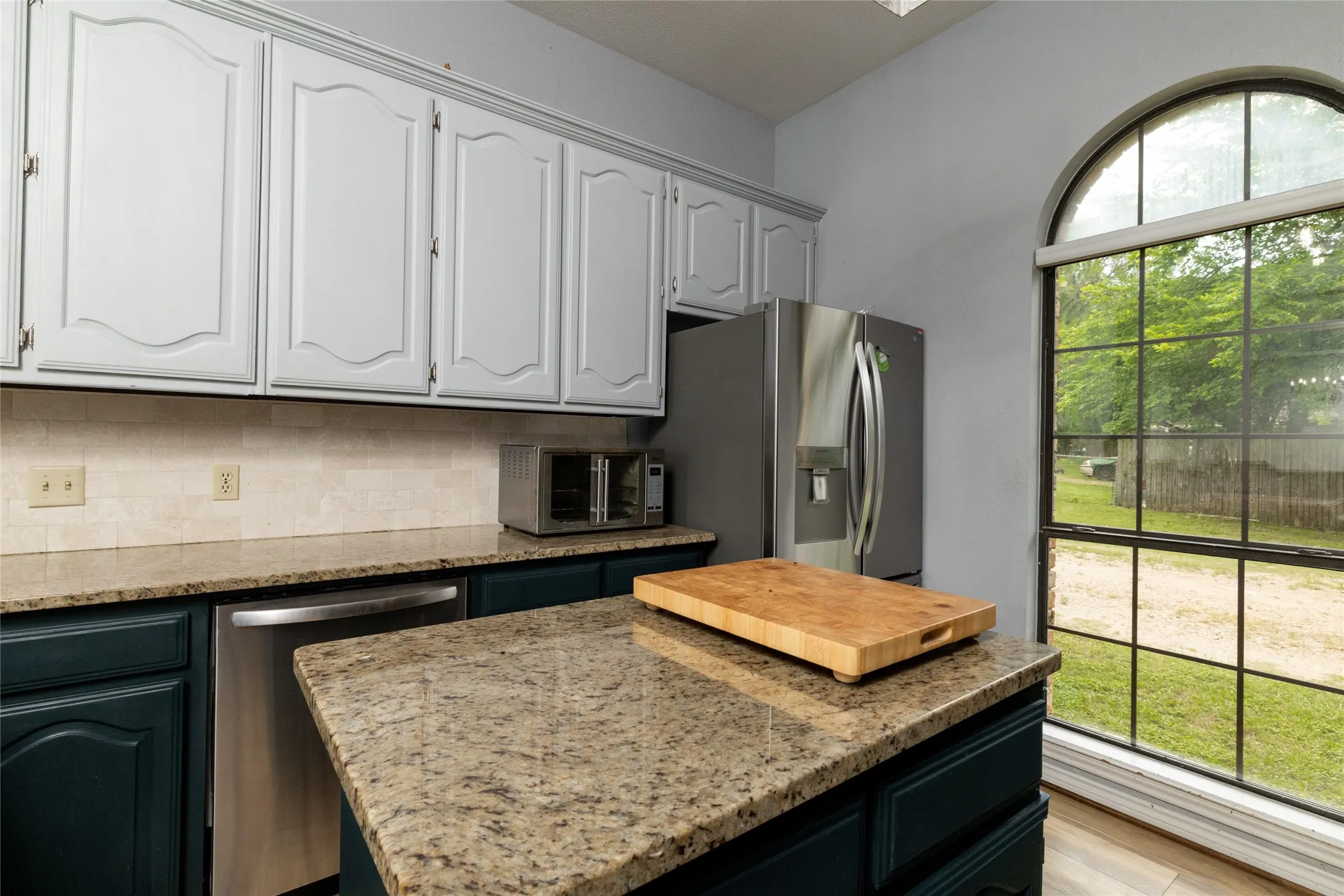 Kitchen featuring two-tone cabinetry, stainless steel appliances, a tile backsplash, and granite countertops