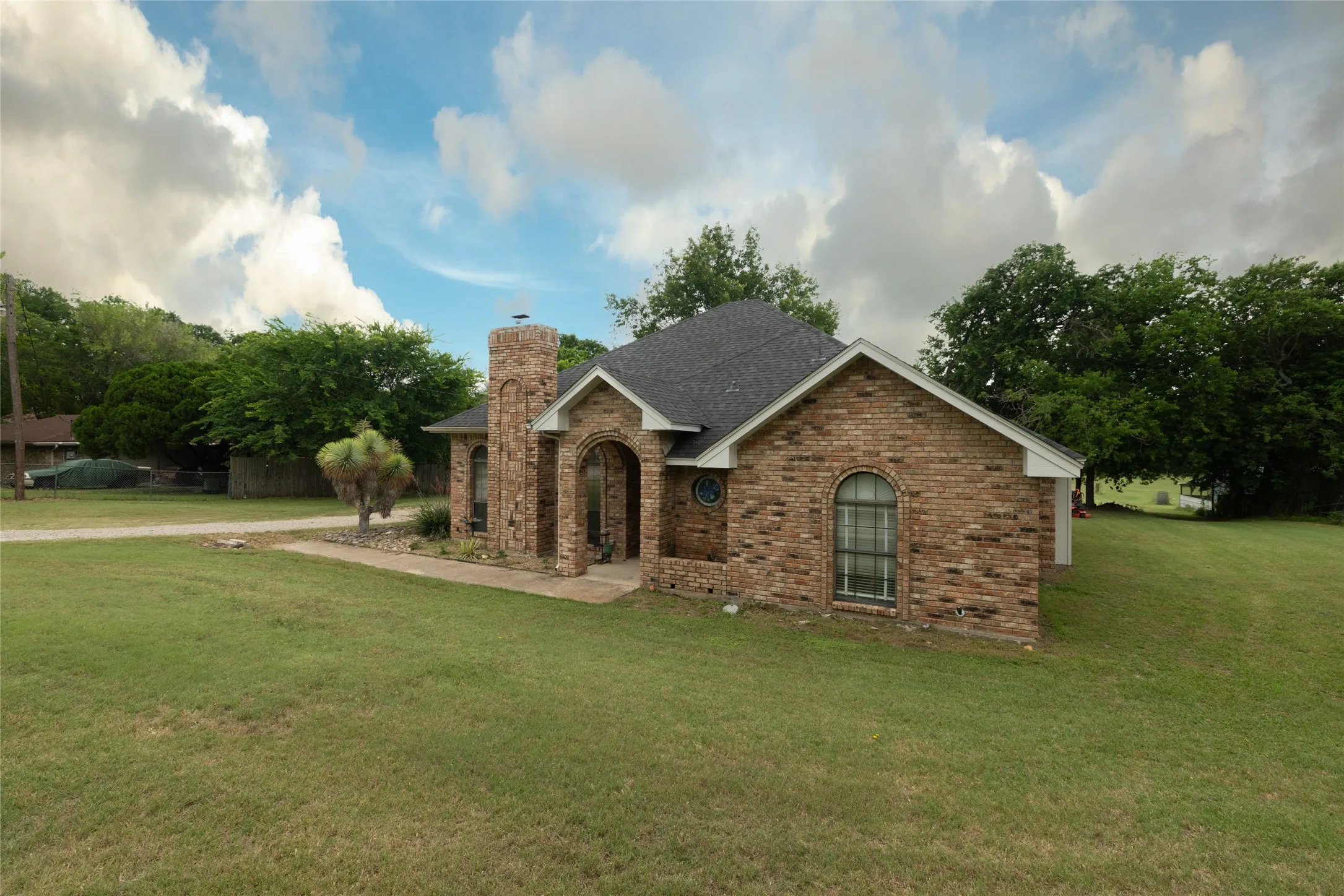 Brick exterior with arched entry, complementing arched windows, a prominent brick chimney, and a dark shingle roof, set on a graded lawn