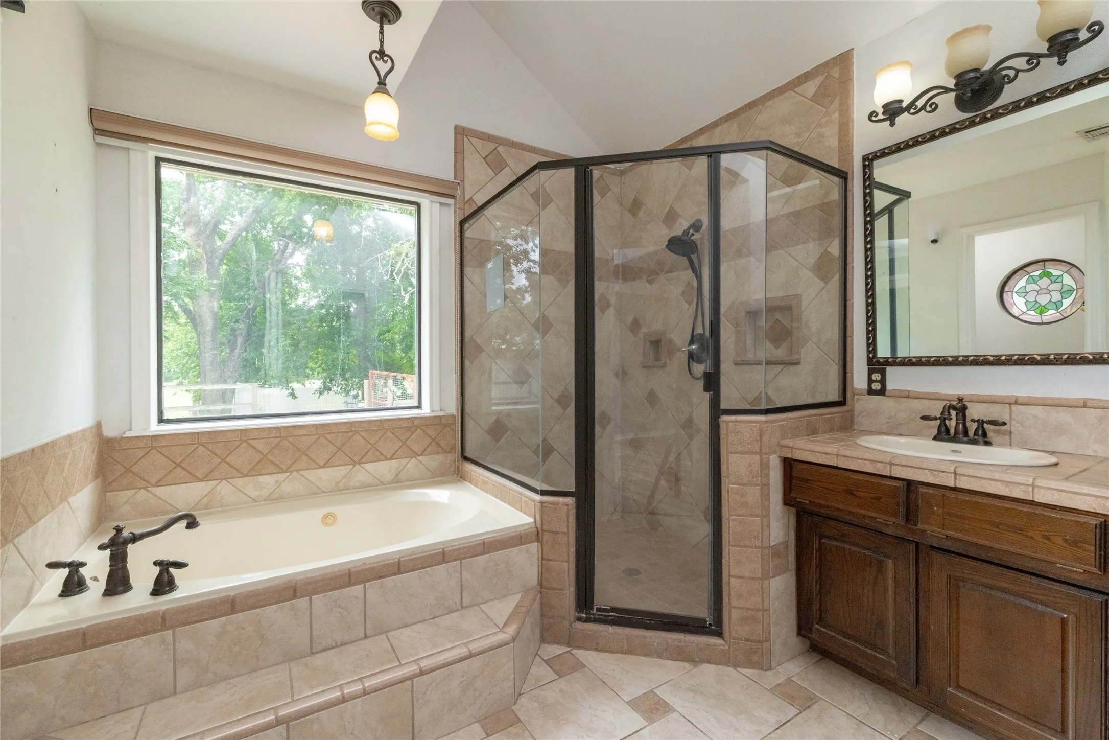 Bathroom featuring a tiled soaking tub with brass fixtures, a walk-in shower with glass enclosure, a single vanity with wood-finish cabinetry, and a framed mirror with overhead lighting