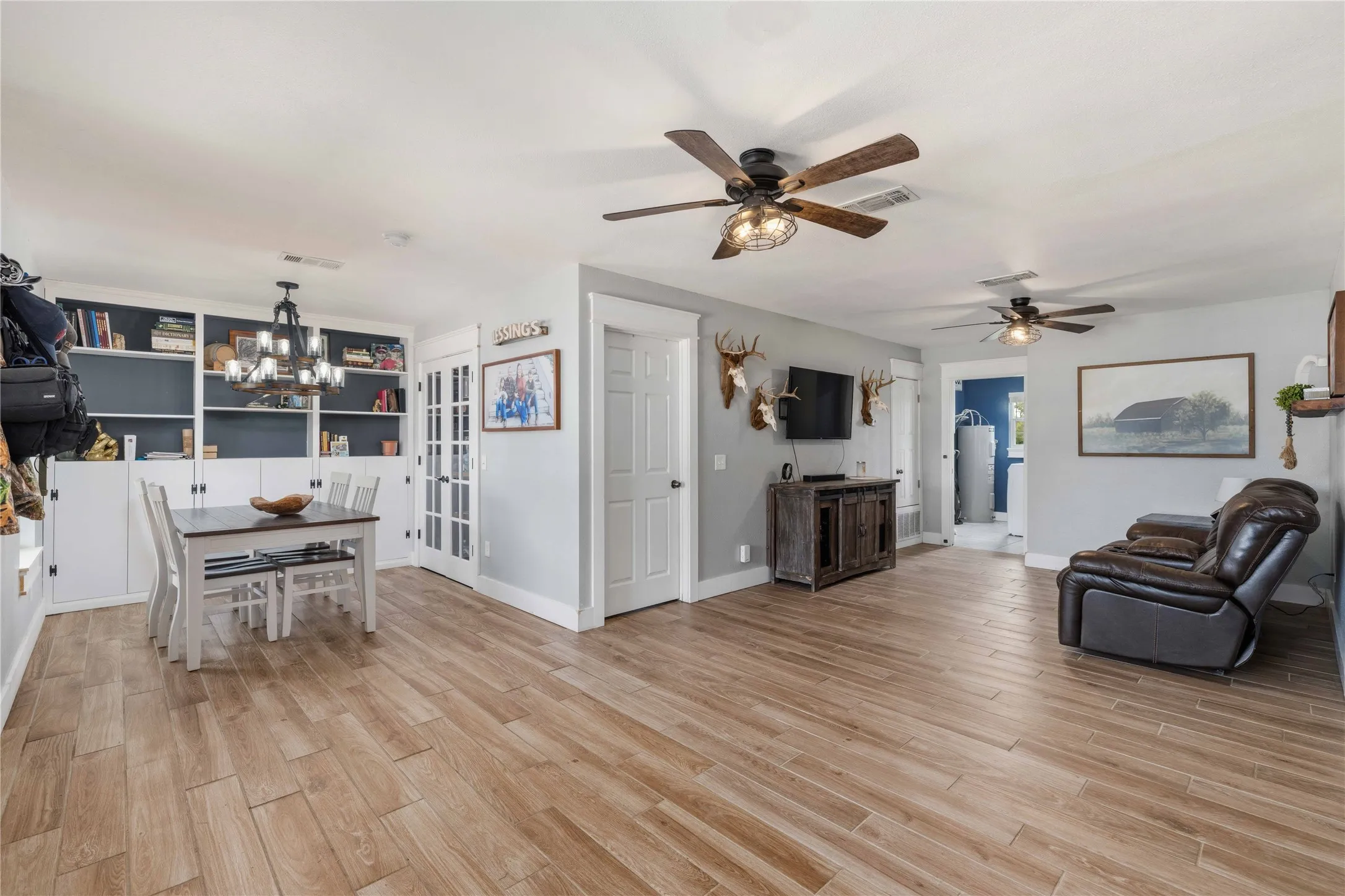 Open-concept living space featuring wood-finish flooring, built-in shelving, a chandelier, and ceiling fans