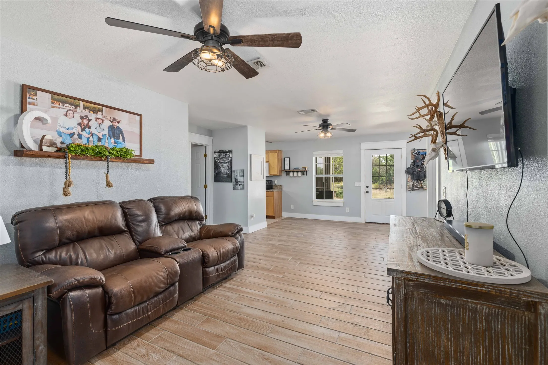 Spacious living area featuring wood-finish flooring, light-toned walls, and multiple ceiling fans with integrated lighting