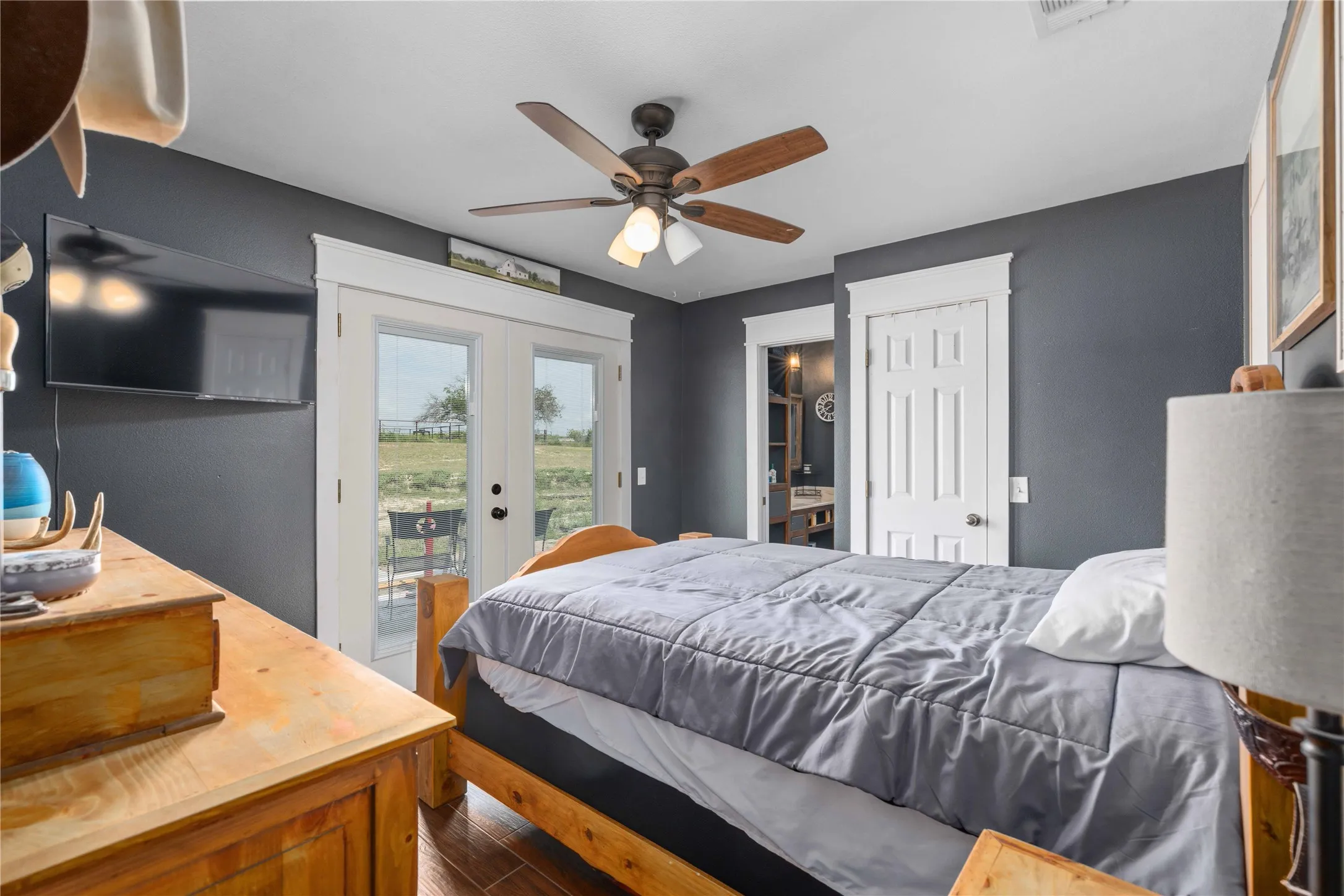Room featuring wood-finish flooring, dark gray walls with white trim, and a ceiling fan with light fixture