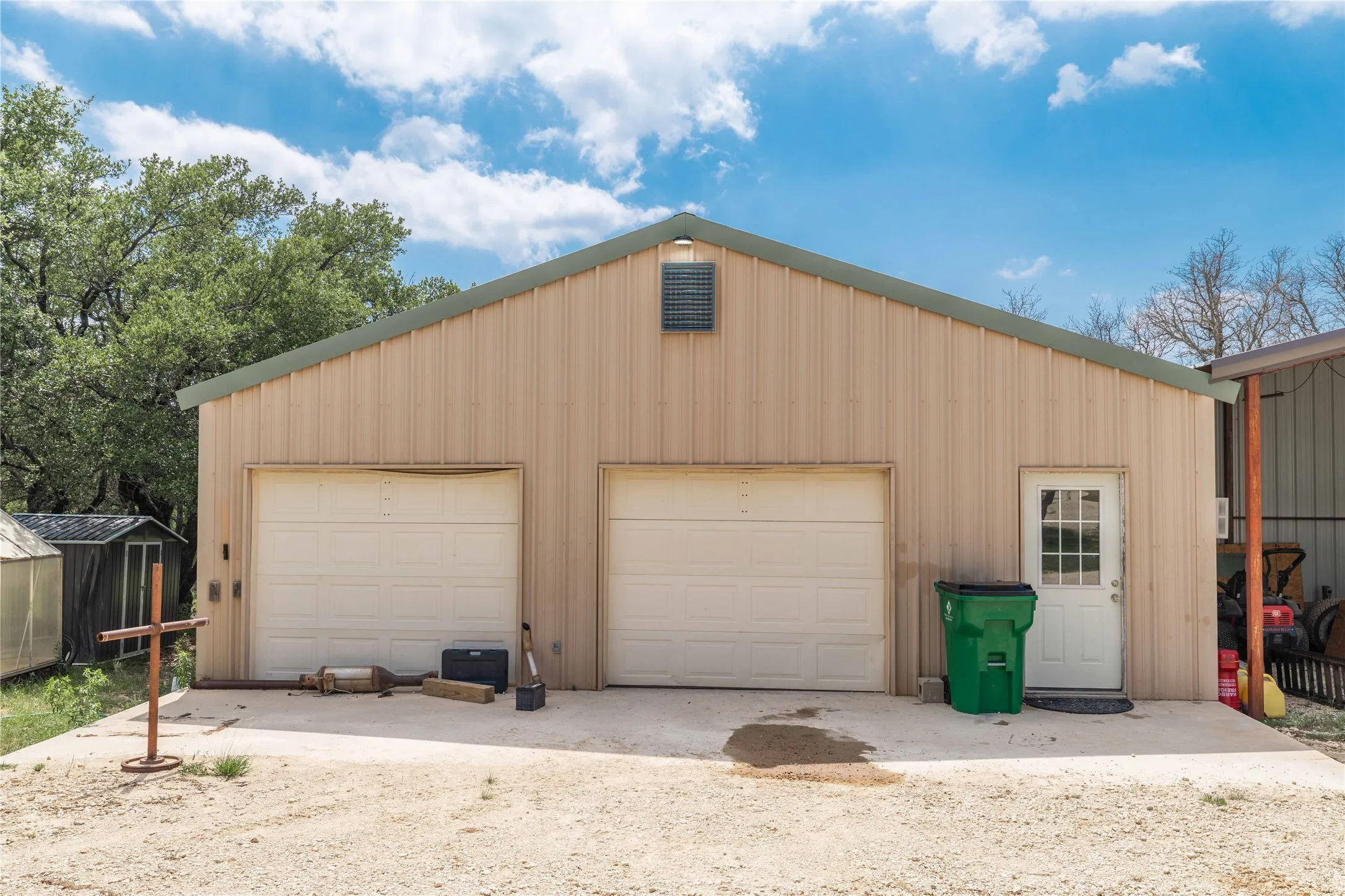 Metal-sided building featuring two garage doors, a pedestrian entry, and a pitched roof with a green trim