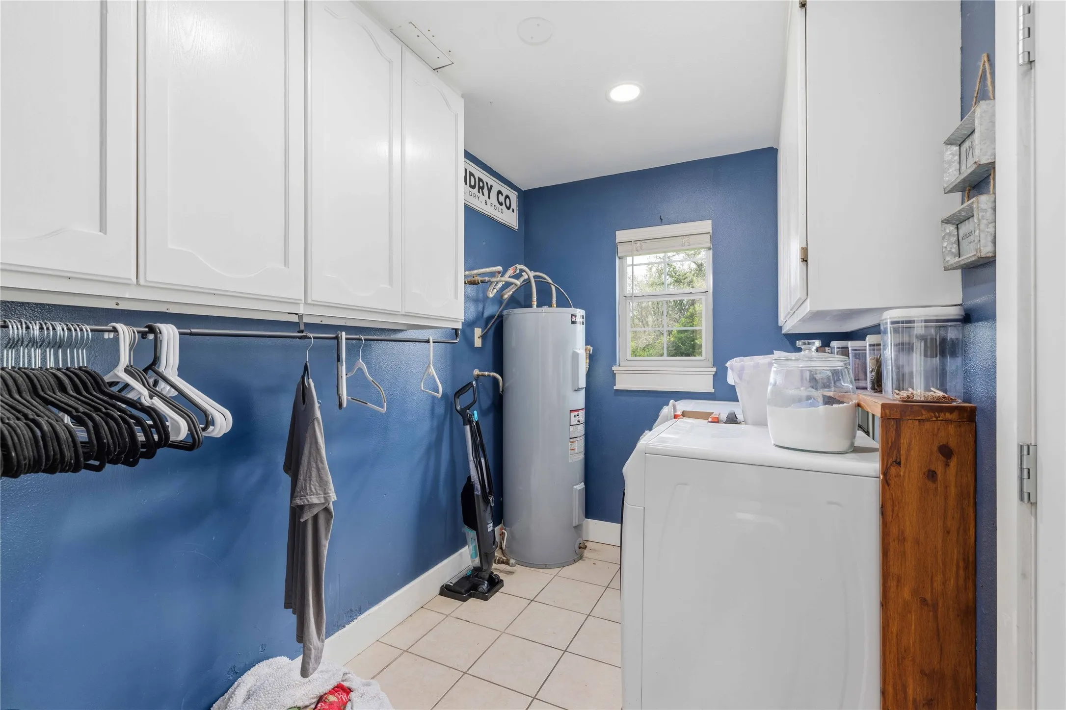 Dedicated utility space featuring white cabinetry, a window with natural light, tile flooring, and a clothes hanging rod