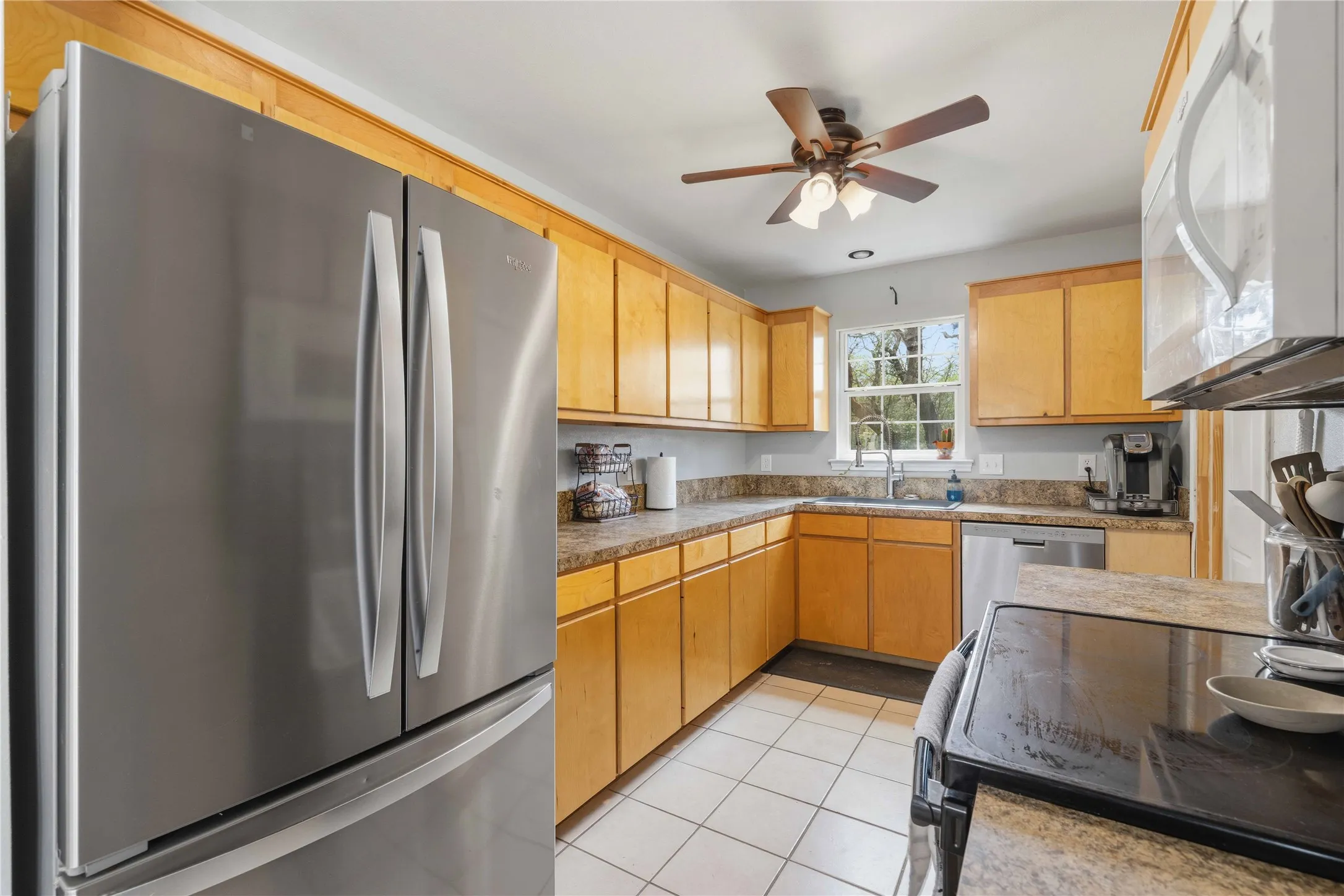 Kitchen featuring stainless steel French door refrigerator, wood cabinetry, L-shaped countertop, stainless steel dishwasher, and a white tile floor