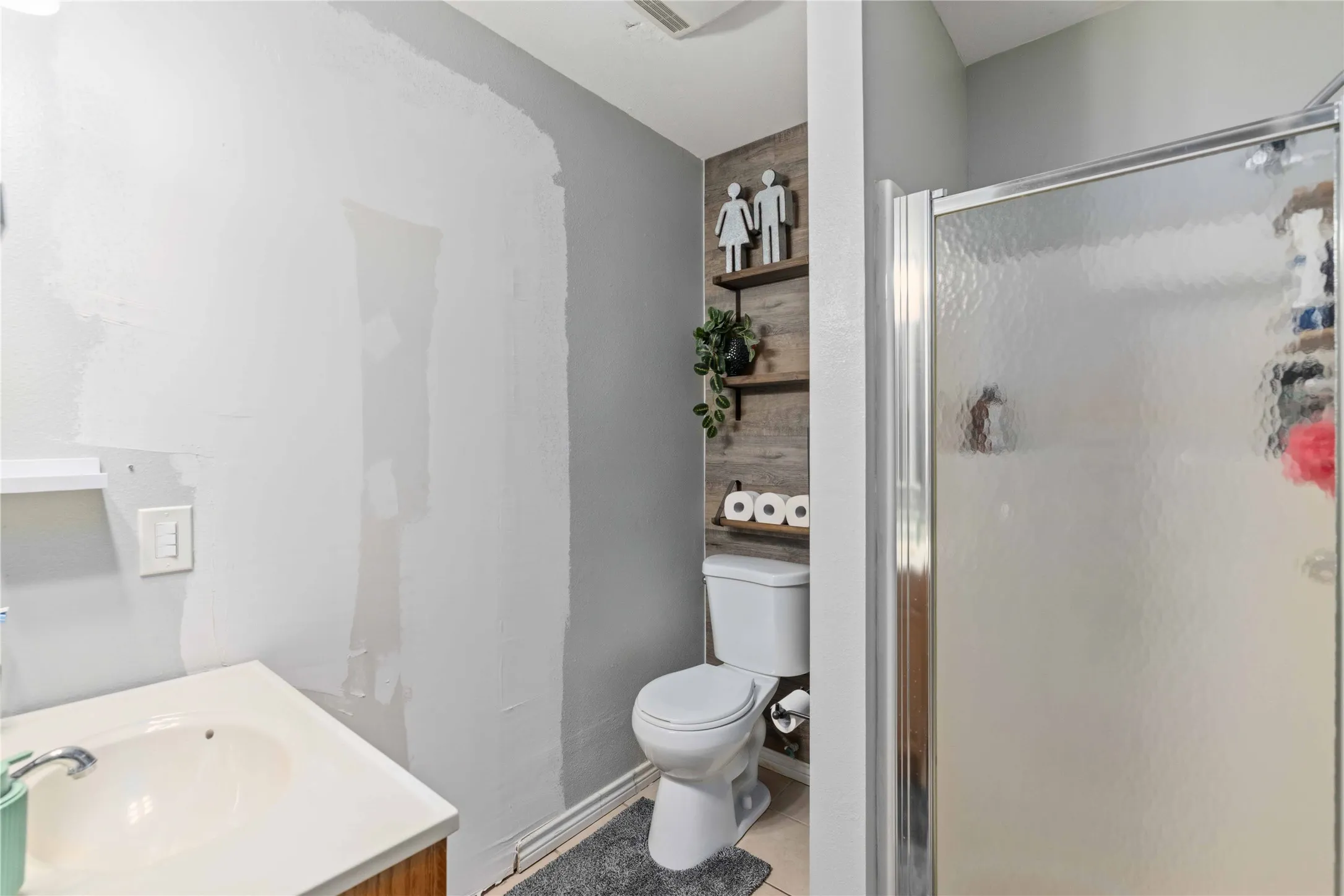 Bathroom featuring a toilet with wood-finish shelving, a shower with a textured glass enclosure, and a vanity with an integrated sink