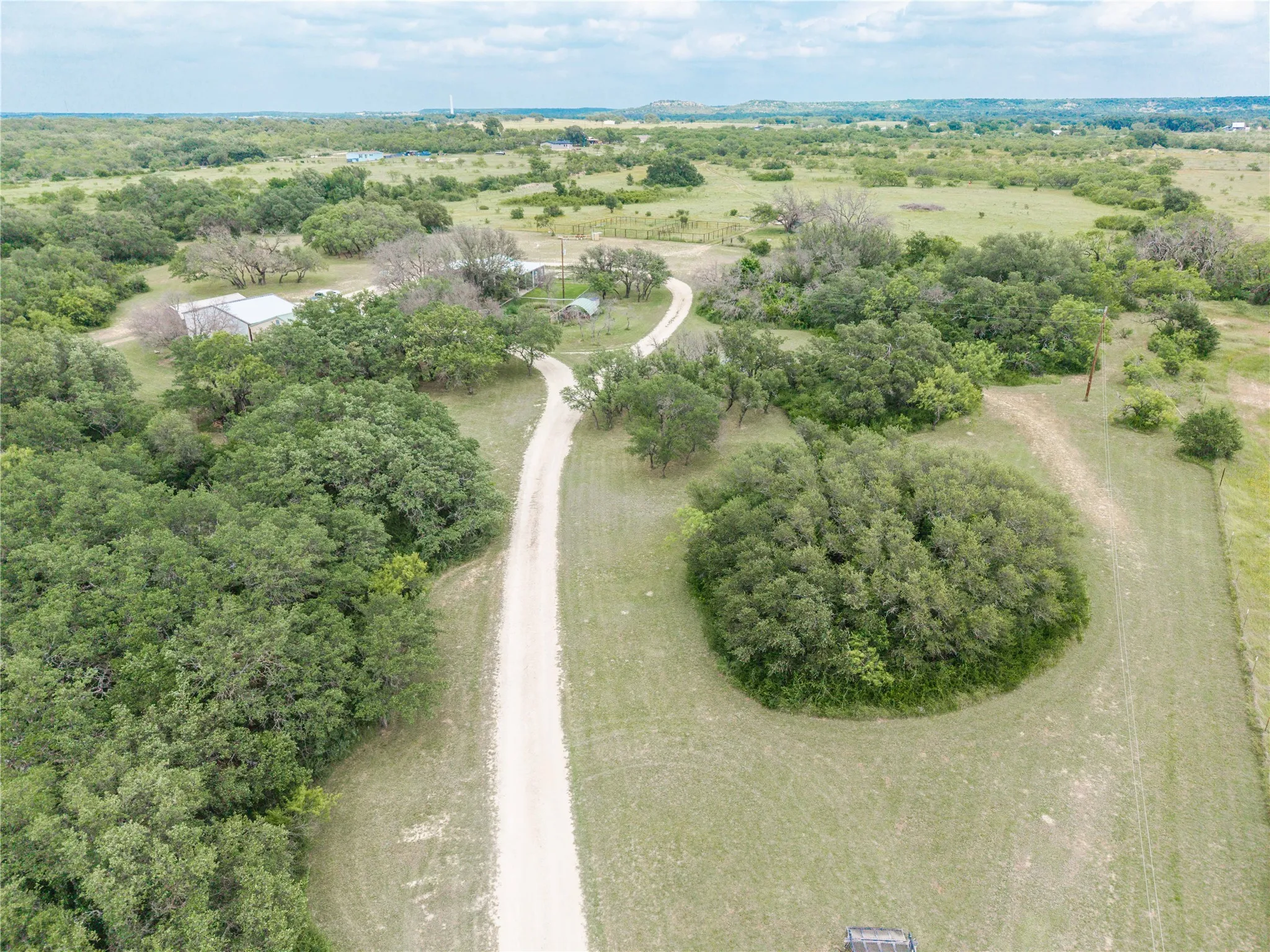 Extensive acreage with a long gravel driveway, mature trees, and multiple structures