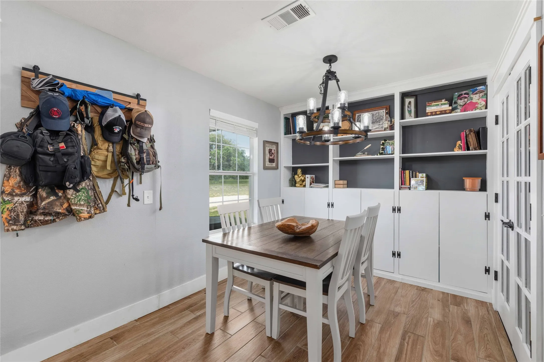 Built-in cabinetry with open shelving and closed storage, wood-finish flooring, a contemporary chandelier, and French doors