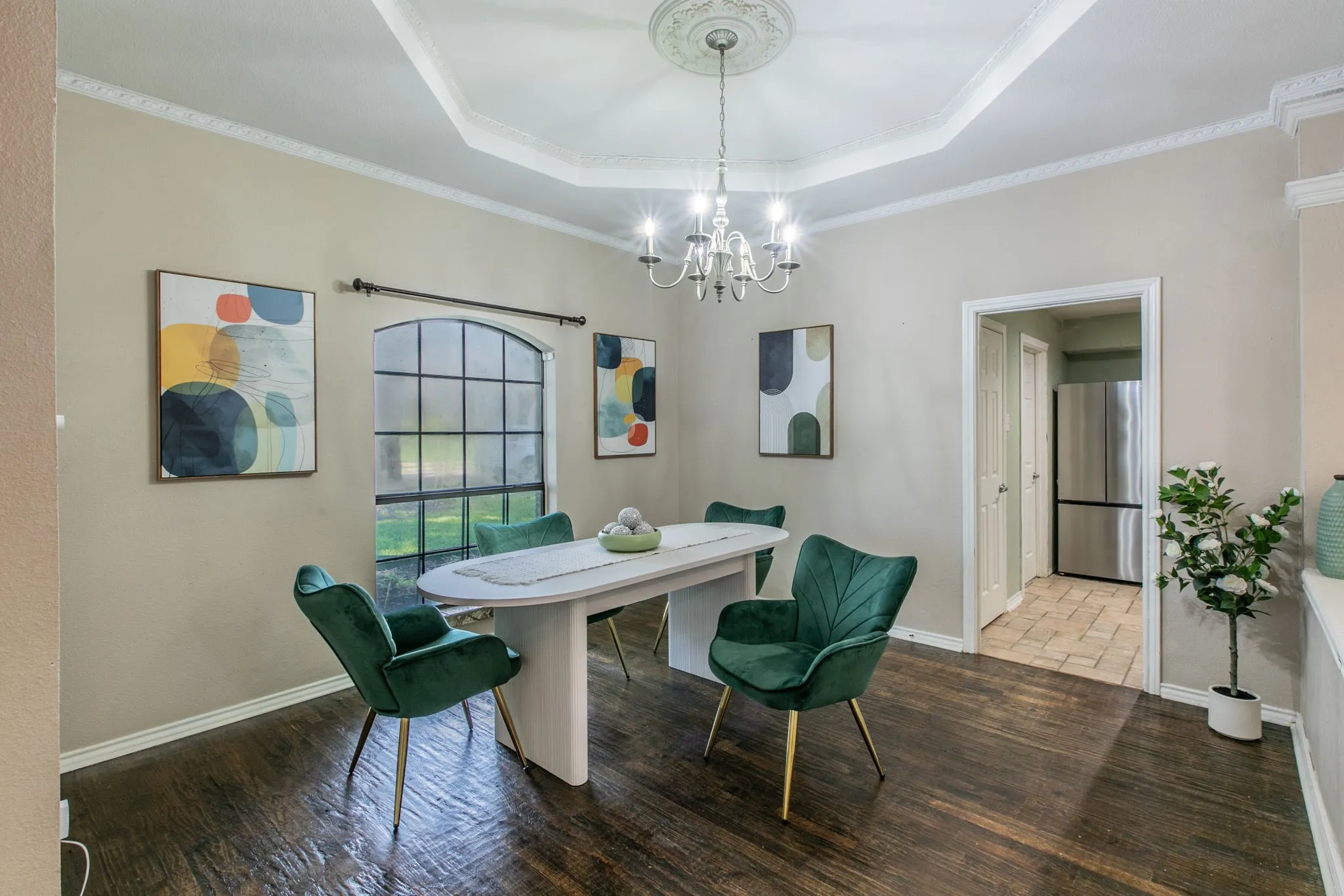 Dining area featuring rich wood-finish flooring, an arched window with grid panes, crown molding, and a tray ceiling with a decorative medallion and chandelier