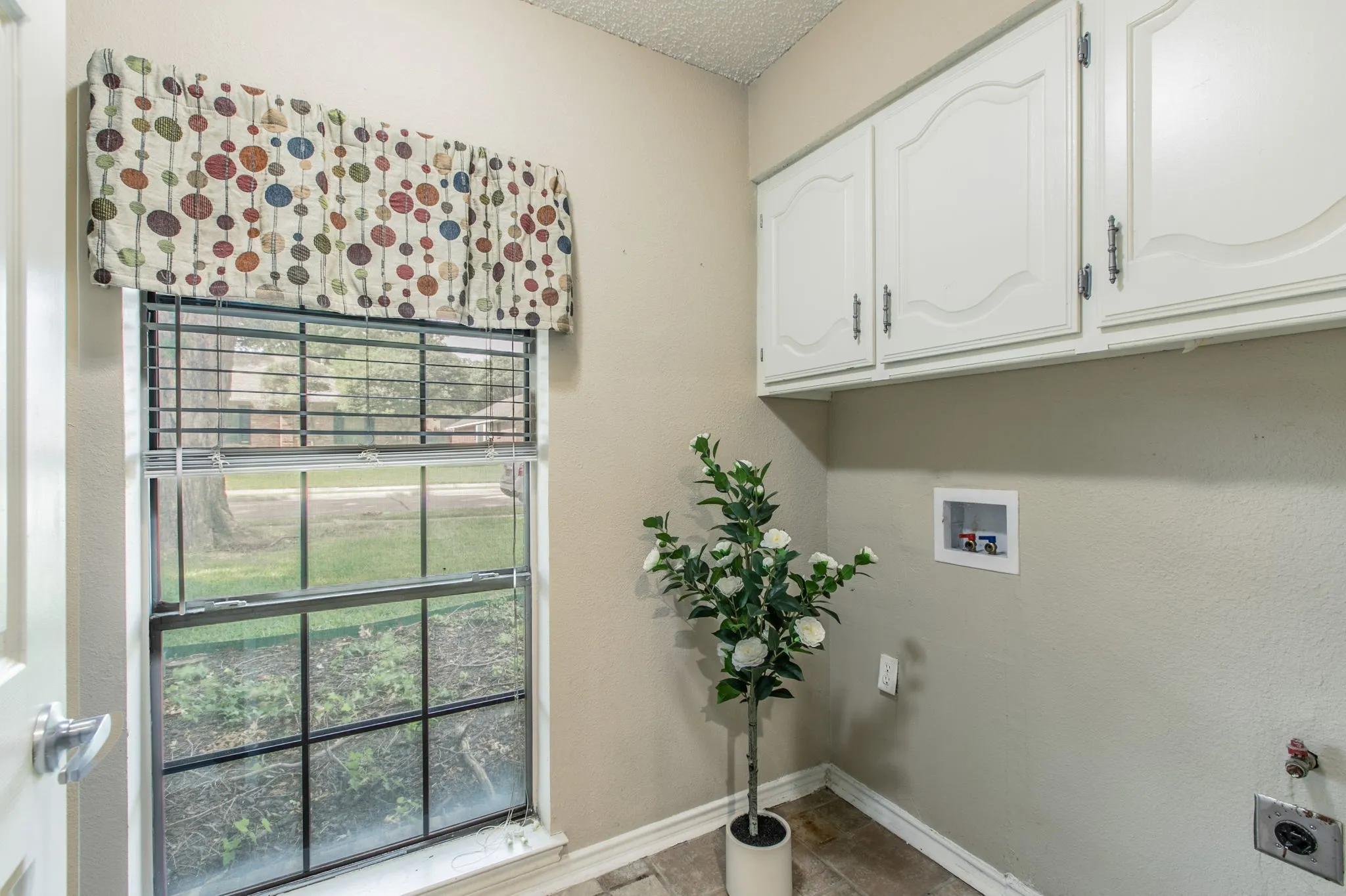 Utility area featuring a window with integrated blinds, upper cabinetry with decorative paneling, and utility hookups for appliances
