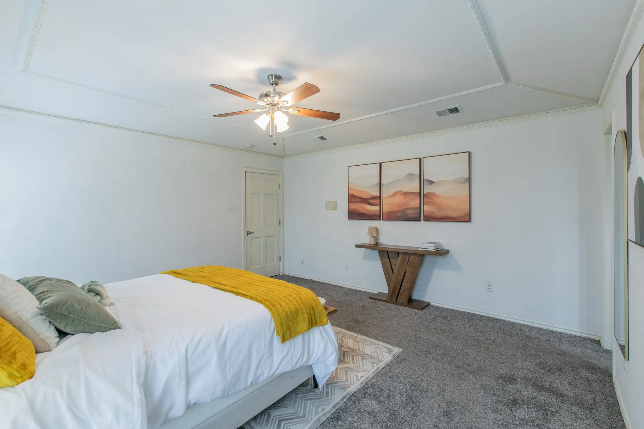 Recessed ceiling with decorative molding, ceiling fan with integrated lighting, door with panel detailing, light-toned walls, and grey carpet flooring