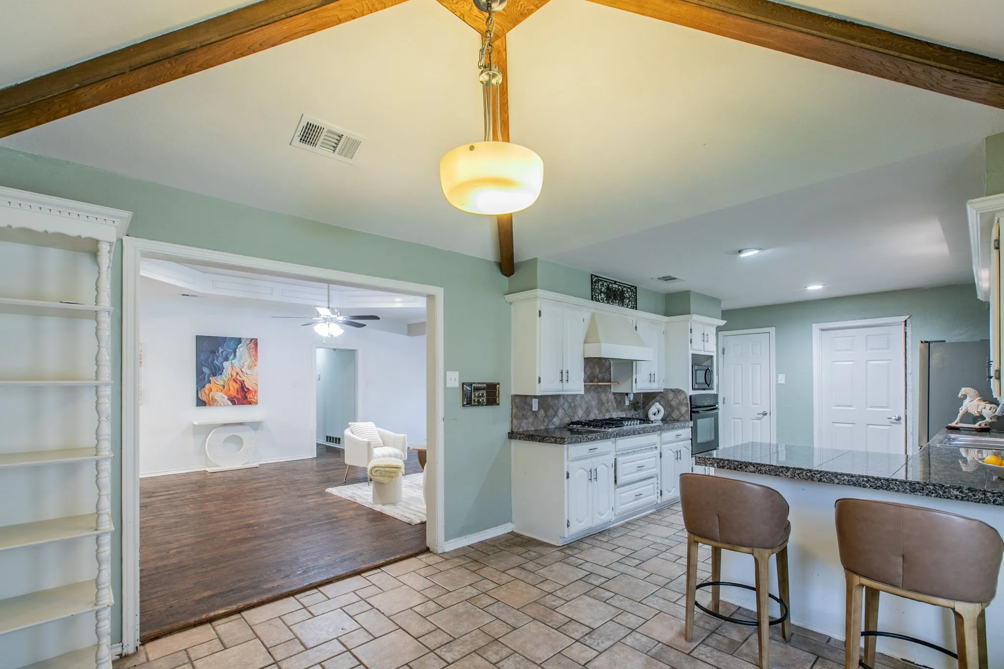 Kitchen featuring tile flooring, white cabinetry, integrated appliances, an island with countertop seating, and exposed wood ceiling beams