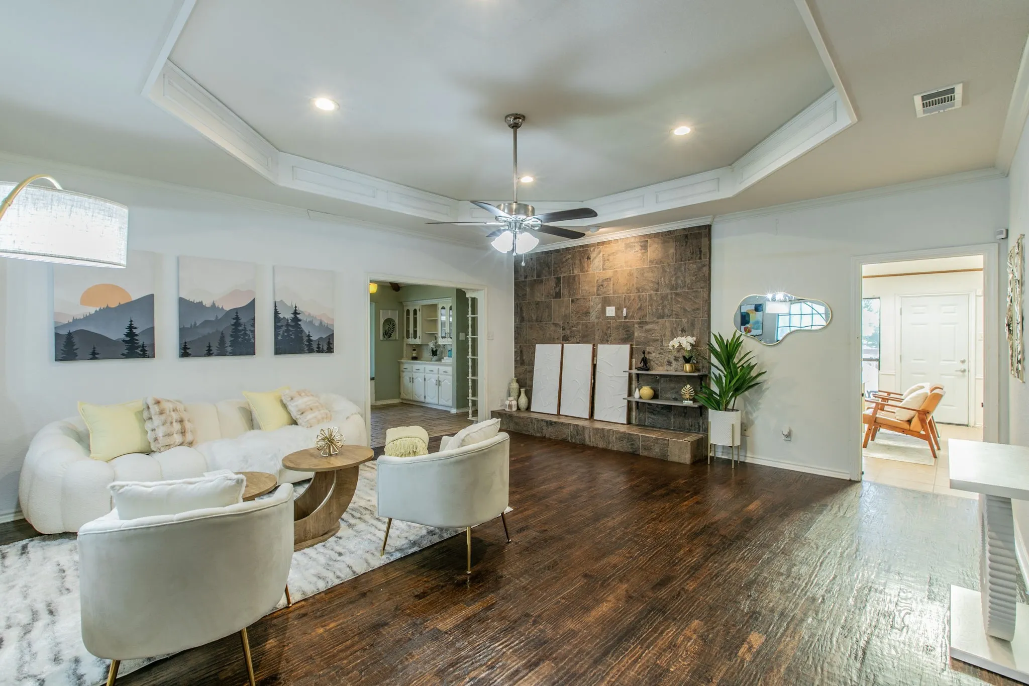 Living area featuring wood-finish flooring, a tray ceiling with recessed lighting, a ceiling fan, and a stone-clad accent wall