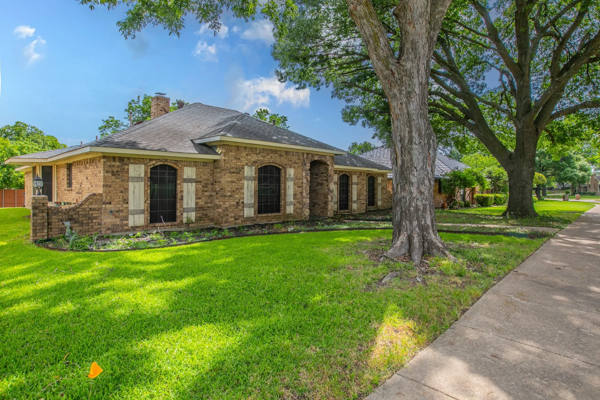 Brick exterior featuring arched windows with decorative shutters, a dark shingle roof, and a prominent chimney