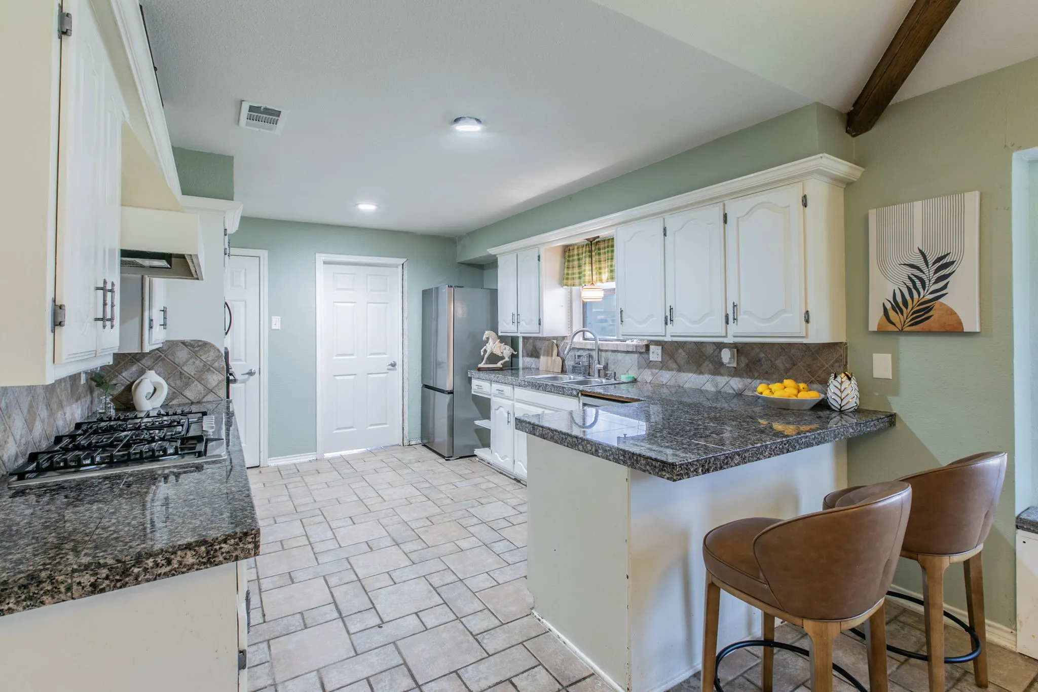 Spacious kitchen featuring granite countertops, a gas cooktop, white cabinetry, a bar-height counter, and tile flooring