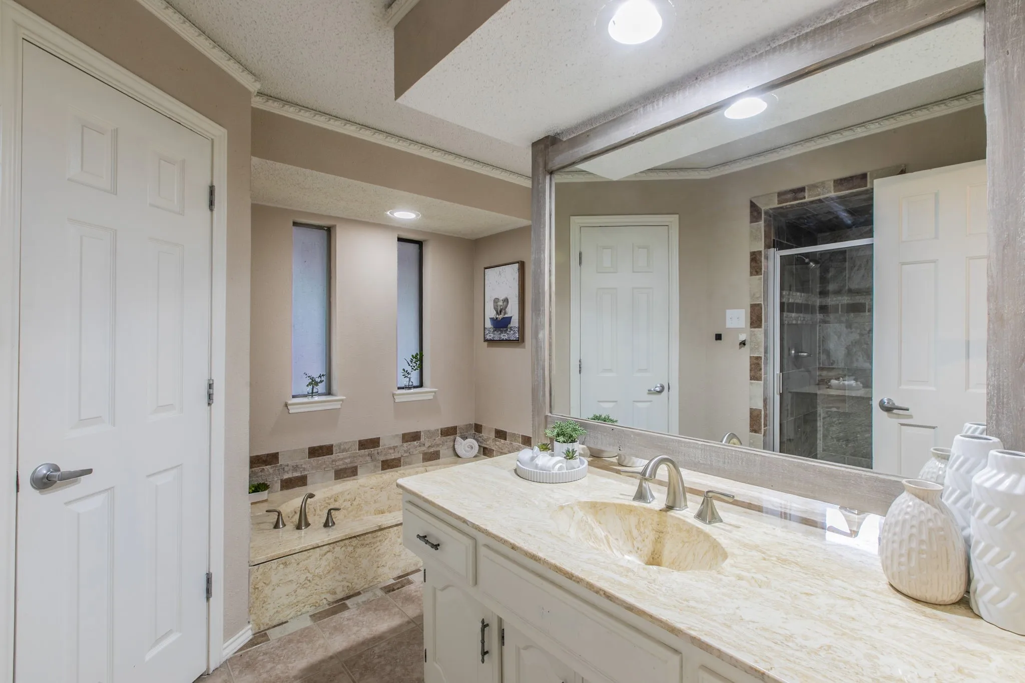 Bathroom featuring a double vanity with stone countertops and integrated basin sinks, a built-in soaking tub with a tiled surround, a walk-in shower with a glass enclosure, and recessed lighting