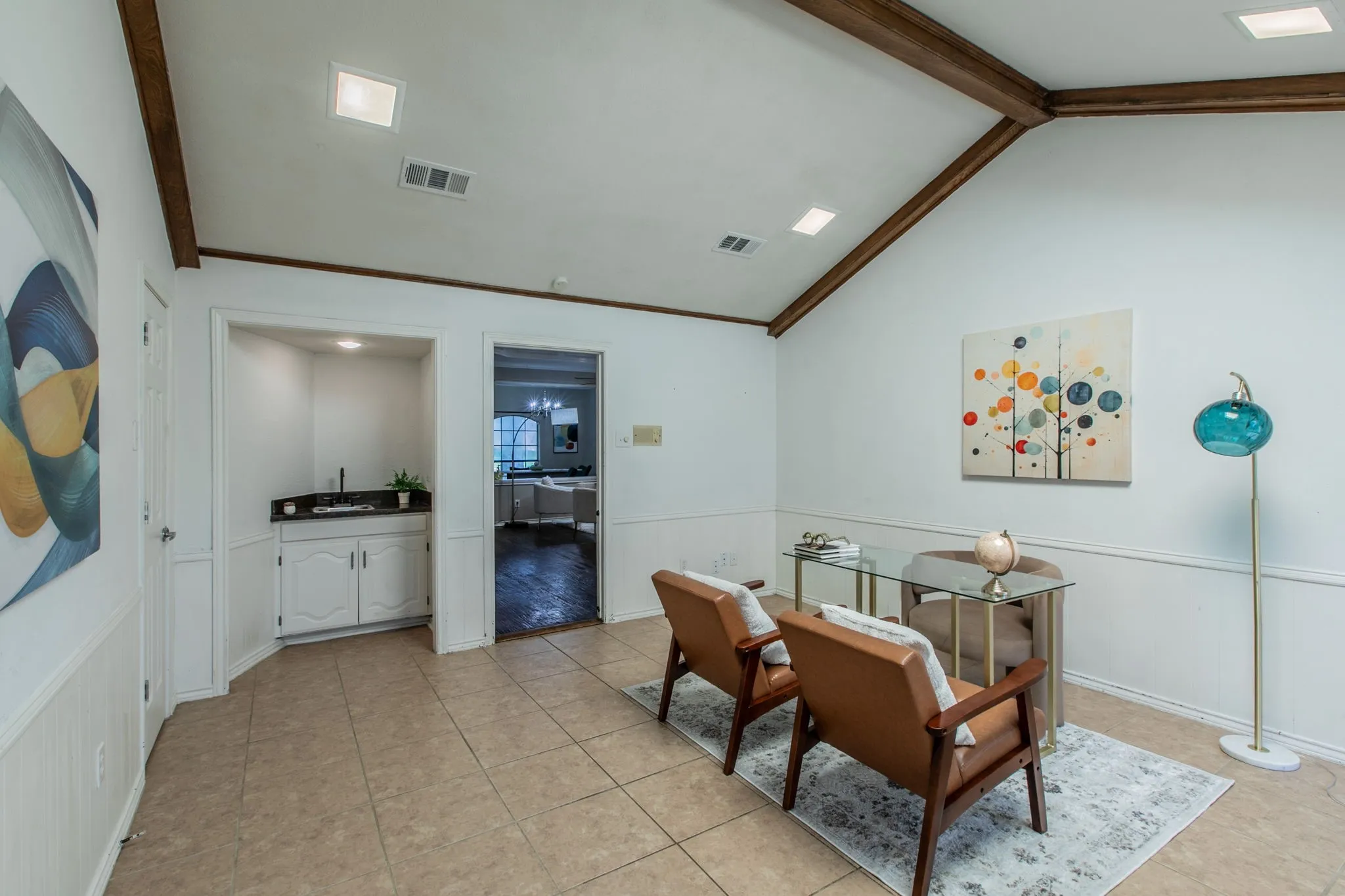Vaulted ceiling with exposed wood beams, tile flooring, and integrated wet bar featuring a dark countertop and white cabinetry