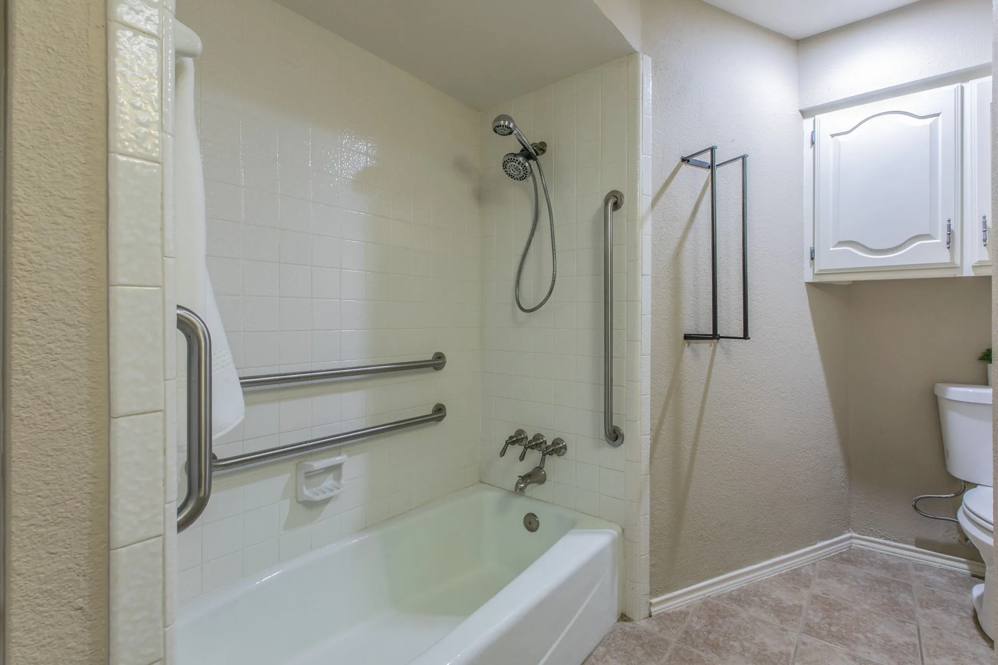 Bathtub and shower combination featuring white subway tile surround, polished chrome fixtures, and integrated grab bars