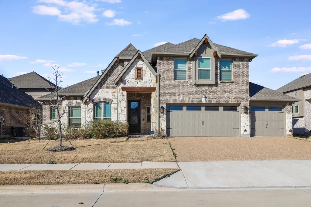 View of front of house featuring stone siding, a garage, roof with shingles, driveway, and brick siding