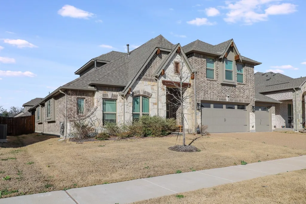 View of front of property featuring an attached garage, brick siding, stone siding, roof with shingles, and a front lawn