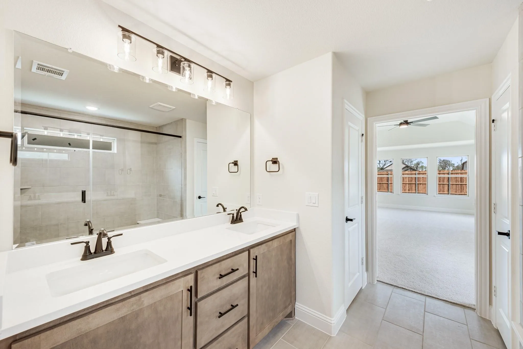 Bathroom featuring a stall shower, double vanity, light tile patterned flooring, and ceiling fan