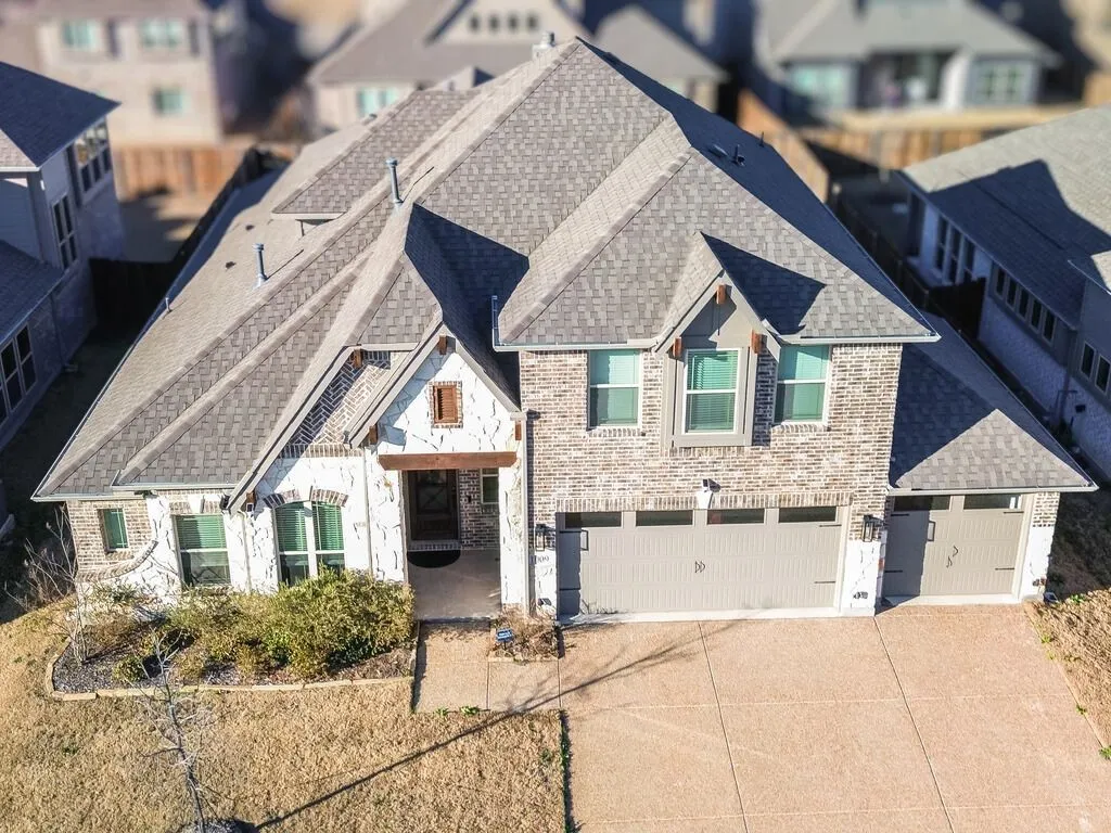 Drone View of front of home featuring roof with shingles, an attached garage, driveway, and a residential view