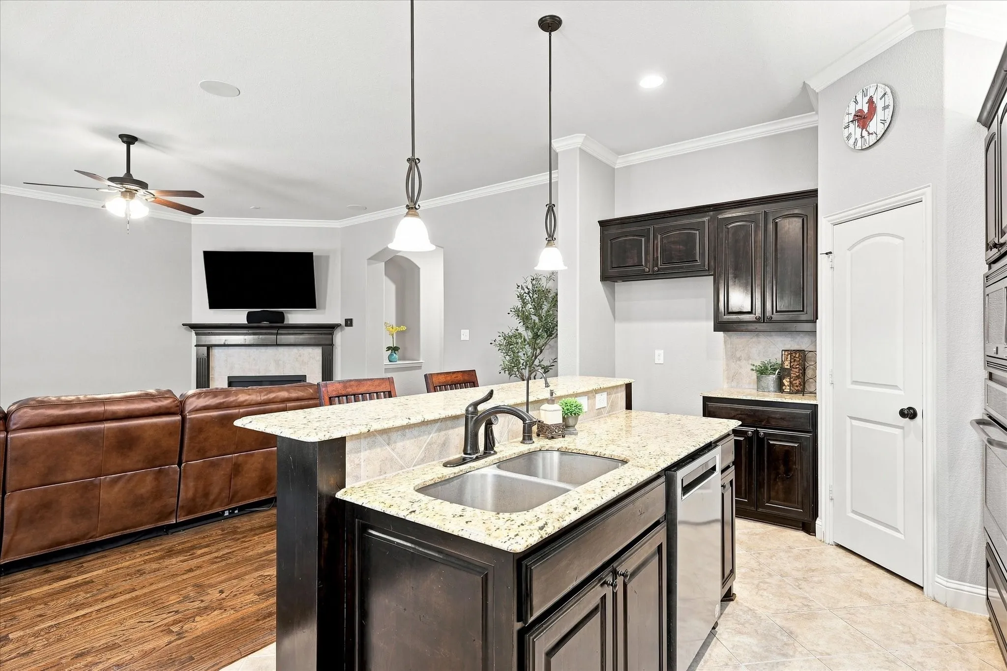 Kitchen island with a double basin stainless steel sink, granite countertops, and dark wood cabinetry