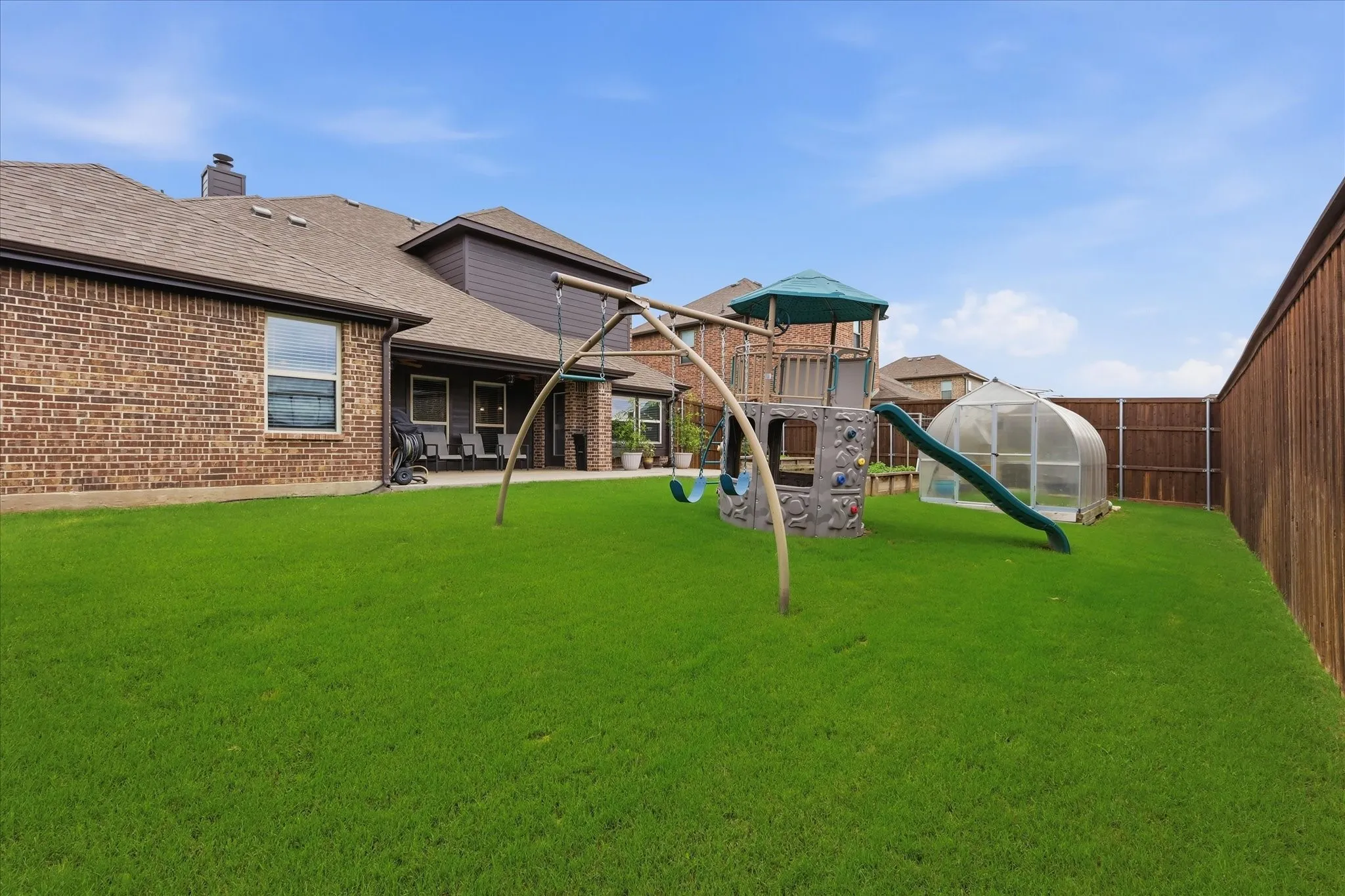 Spacious backyard featuring a manicured lawn, a full wooden privacy fence, and a covered patio area