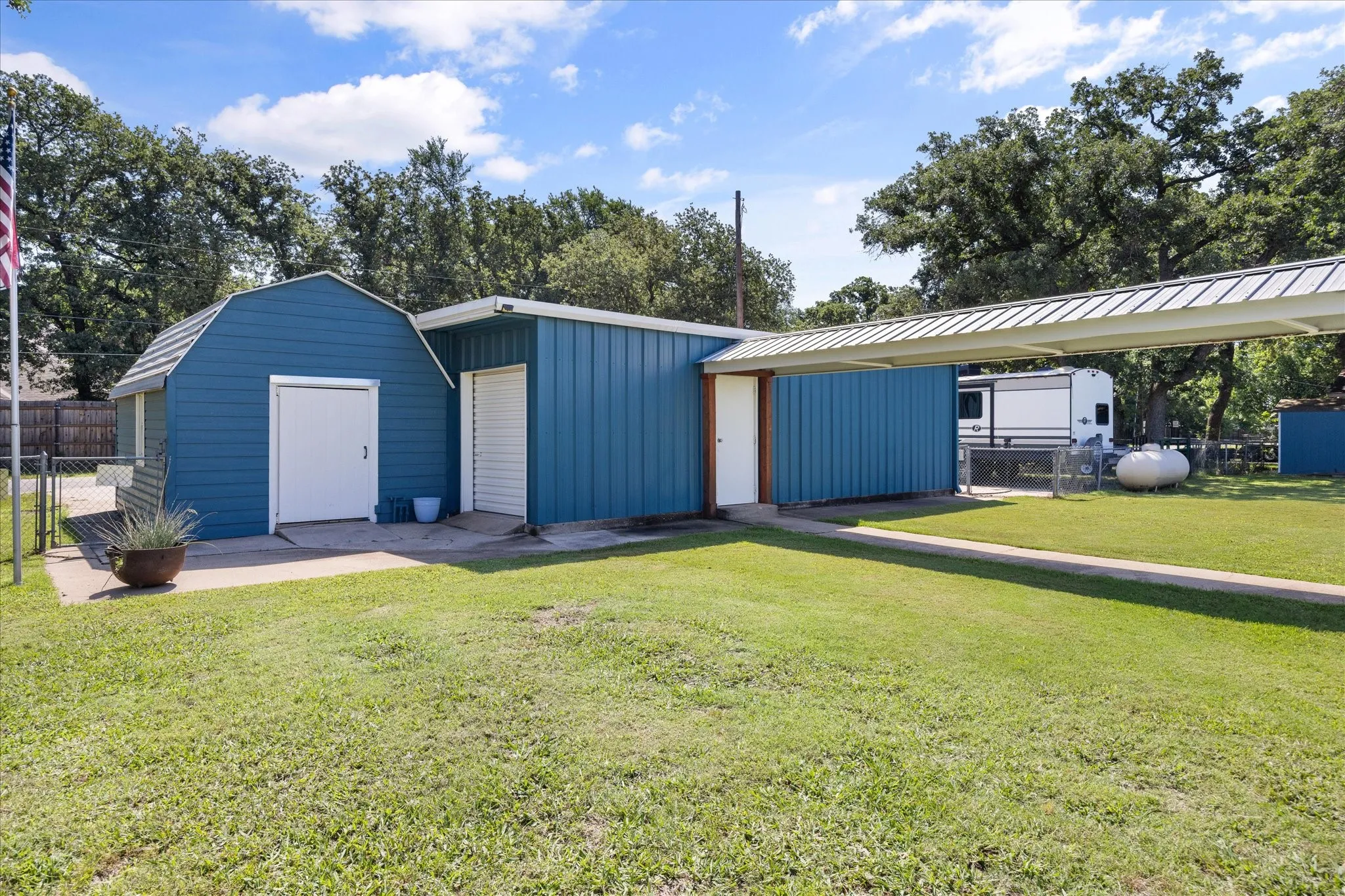 Blue-paneled outbuilding with a gambrel roof and an adjacent metal carport structure
