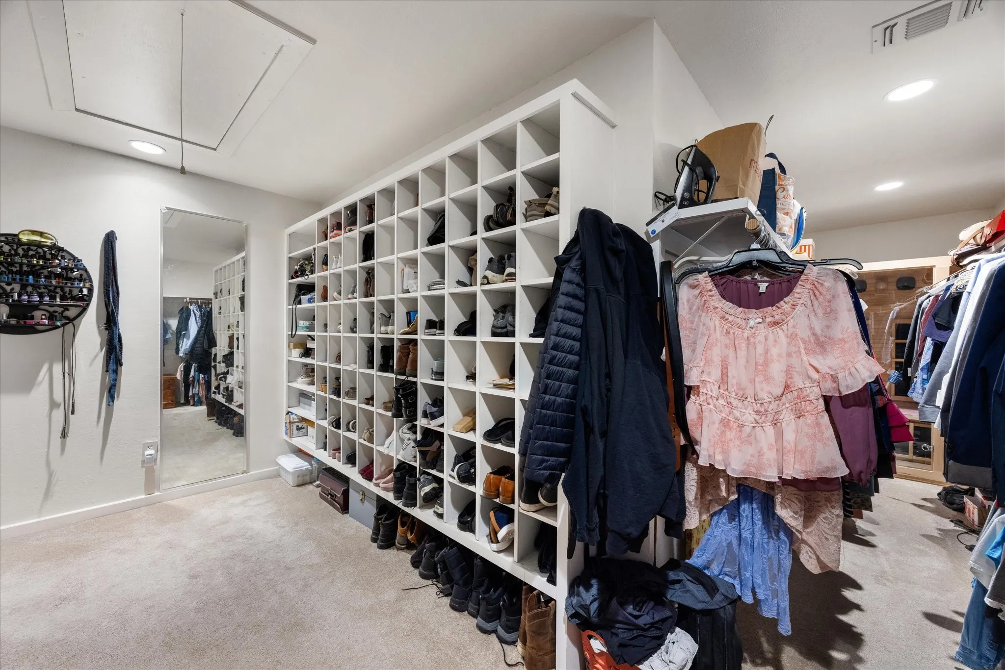 Built-in shelving and storage systems in a carpeted room with recessed lighting and a full-length mirror